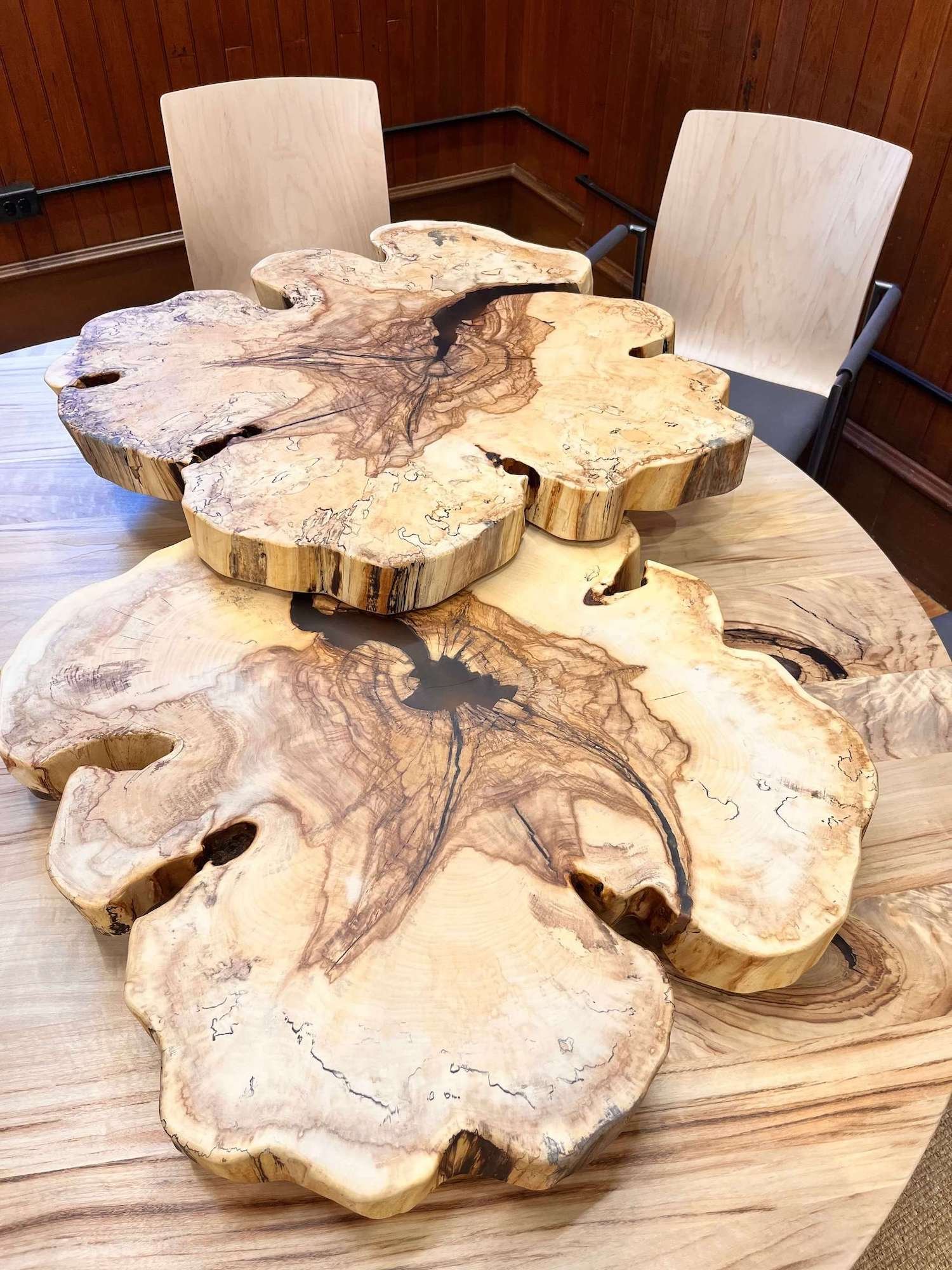 A set of natural horse chestnut tables with irregular shapes and dark streaks, placed on a wooden floor in a room at Shelburne Farms.