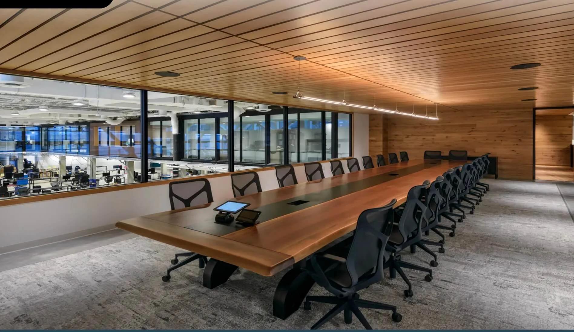 Modern conference room with a 20 foot long black walnut table, black ergonomic chairs, and a large window overlooking an open office space at Boston Dynamics.