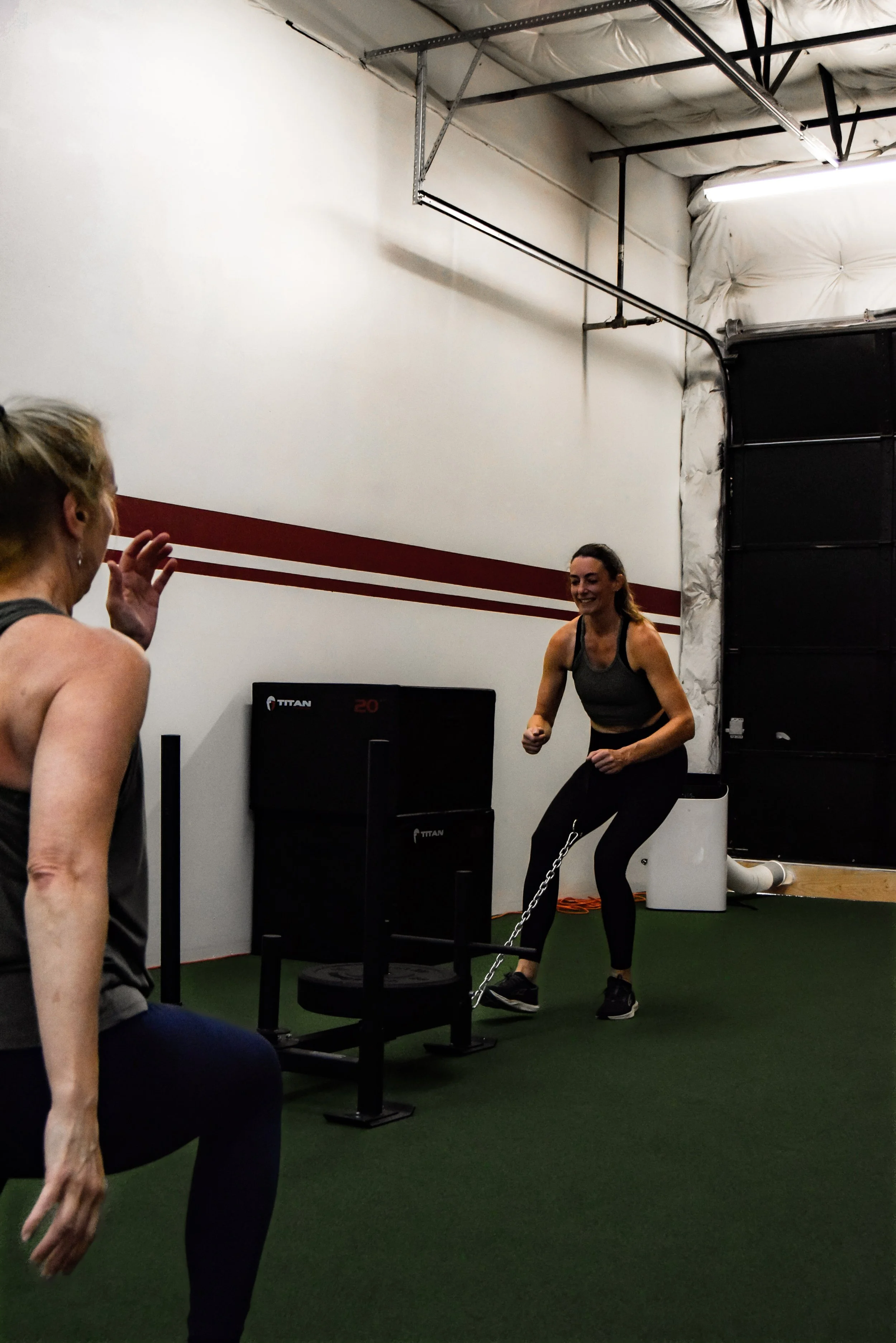 Two people exercising on kettlebells during a workout session at a gym, with a woman in the foreground and a man beside her, both focused on their workout.