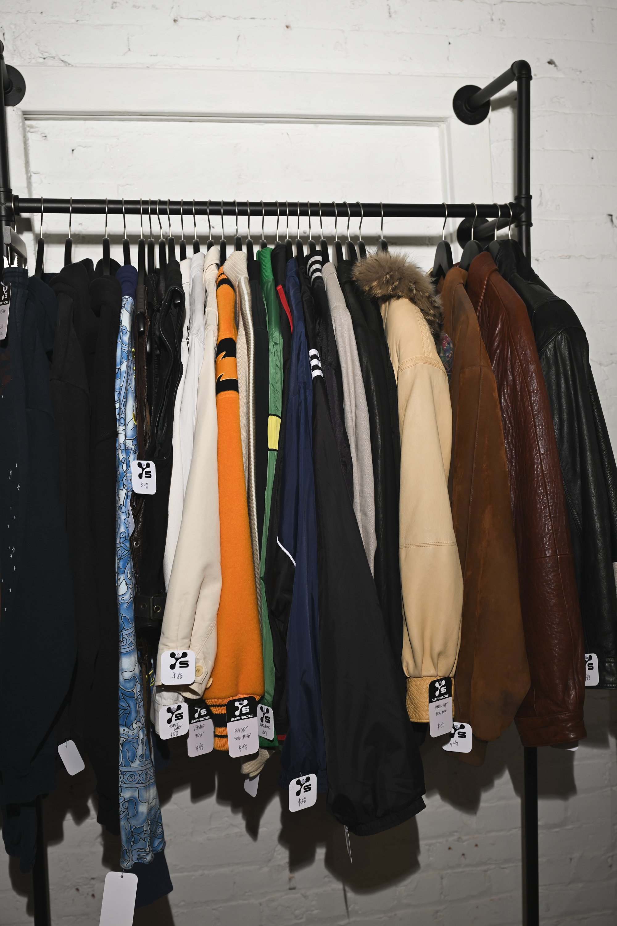 Clothing rack with various jackets, sweaters, and shirts hanging on black hangers in a retail store.