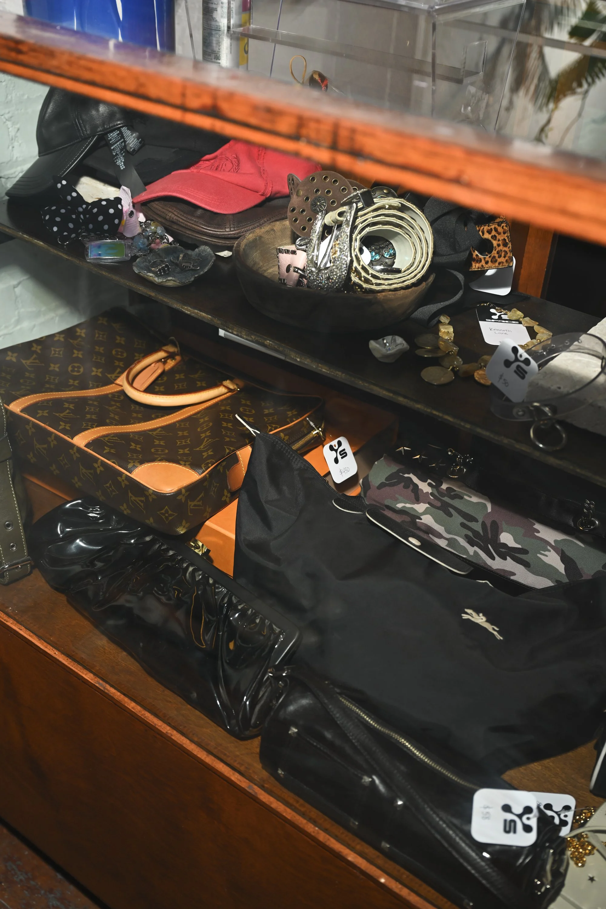 A display case filled with various accessories, including jewelry, belts, hats, and a bag with a Louis Vuitton pattern.