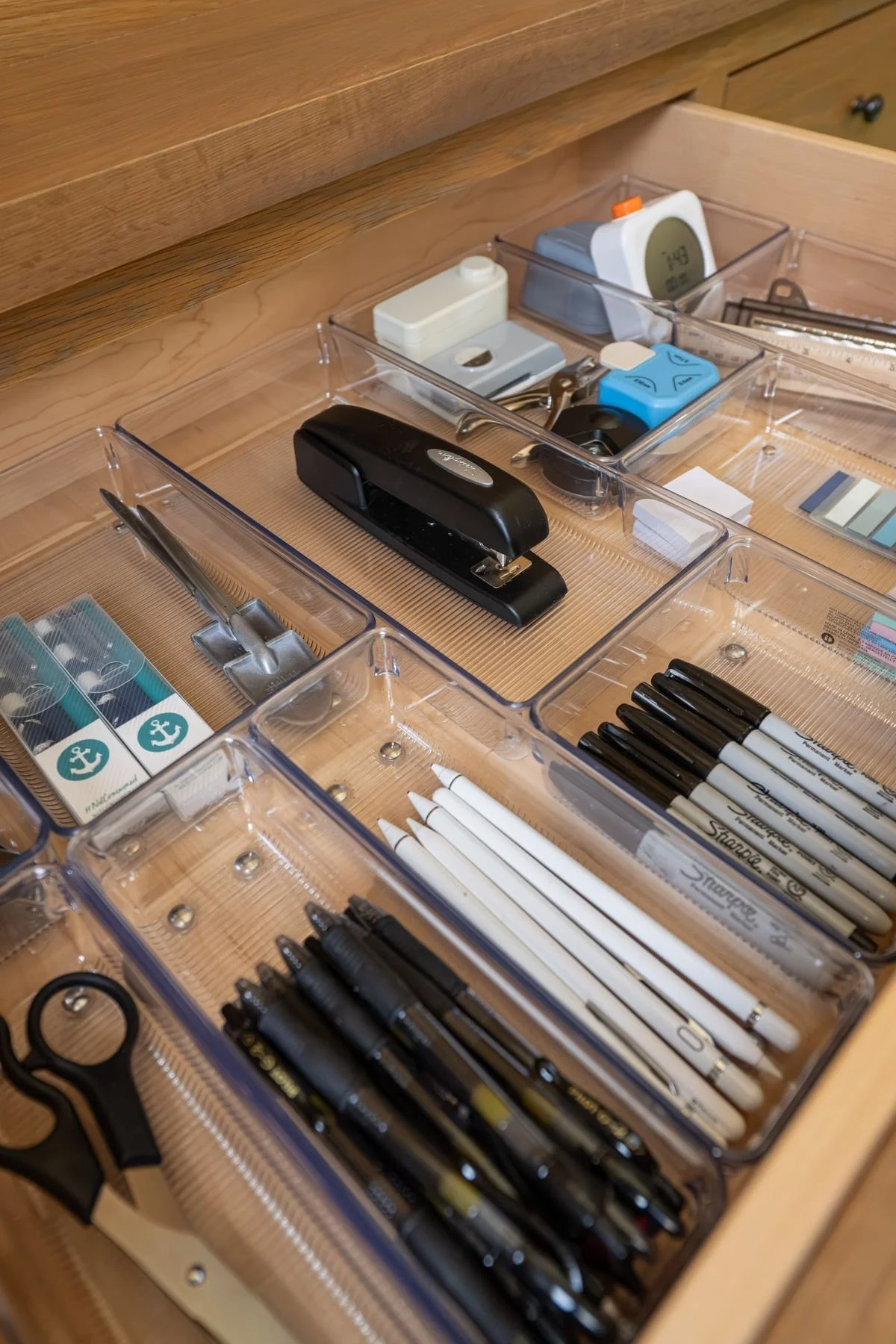 Organized desk drawer containing office supplies including pens, markers, scissors, staples, and correction tape.