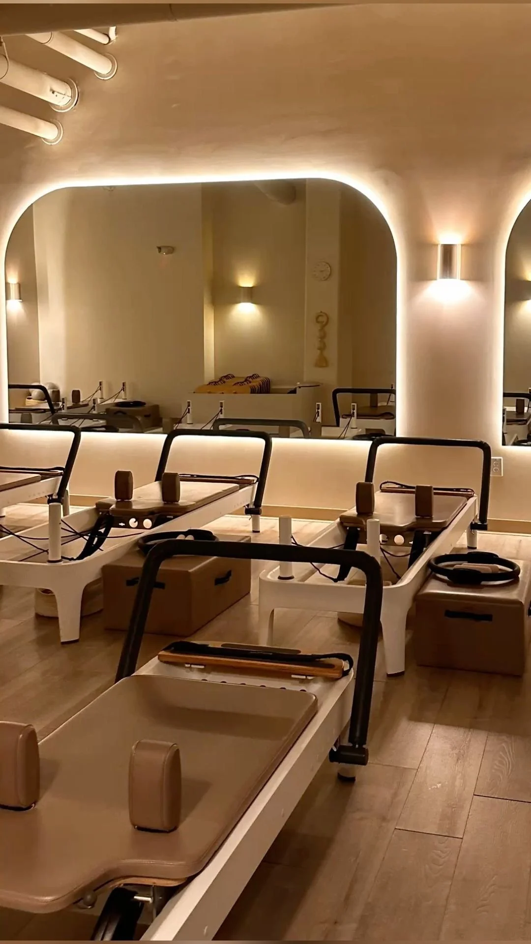 Empty medical or spa treatment beds with head supports in a warm, softly lit room featuring large wall mirror, wall sconces, and decorative wall art.
