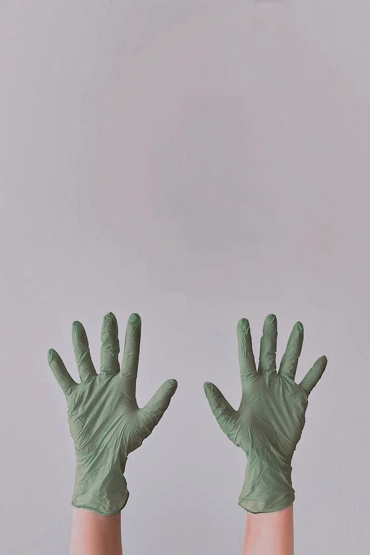 Two hands wearing green disposable gloves are raised against a plain background.