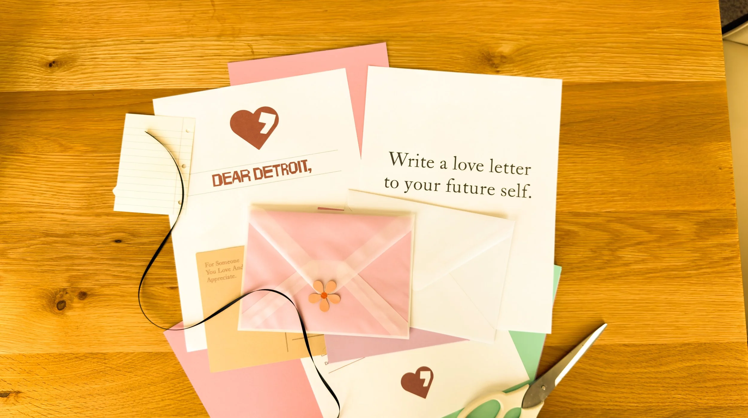 Various love letters and greeting cards on a wooden surface, including one with a heart and the text 'Dear Detroit,' and another with the message 'Write a love letter to your future self.'
