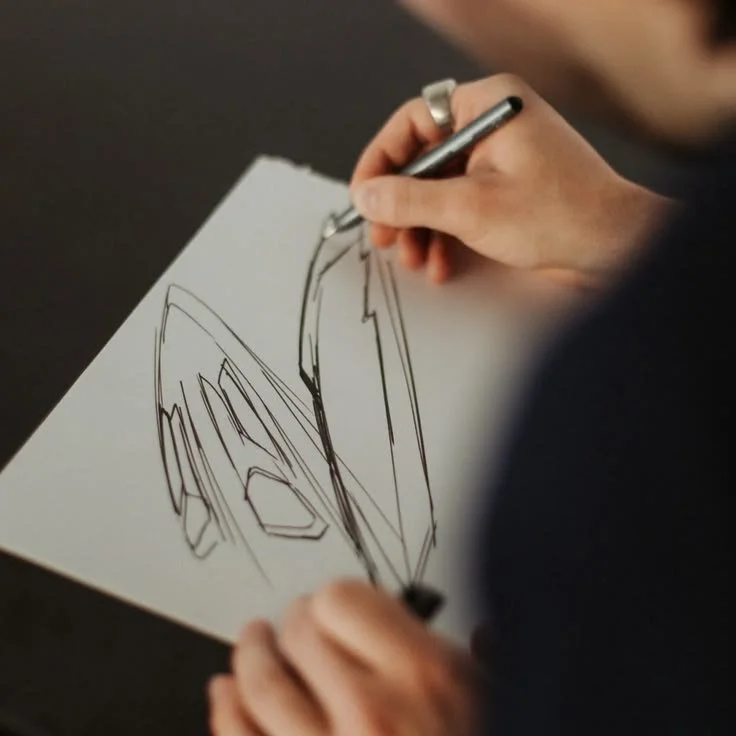 Person sketching a car on white paper with a pen.