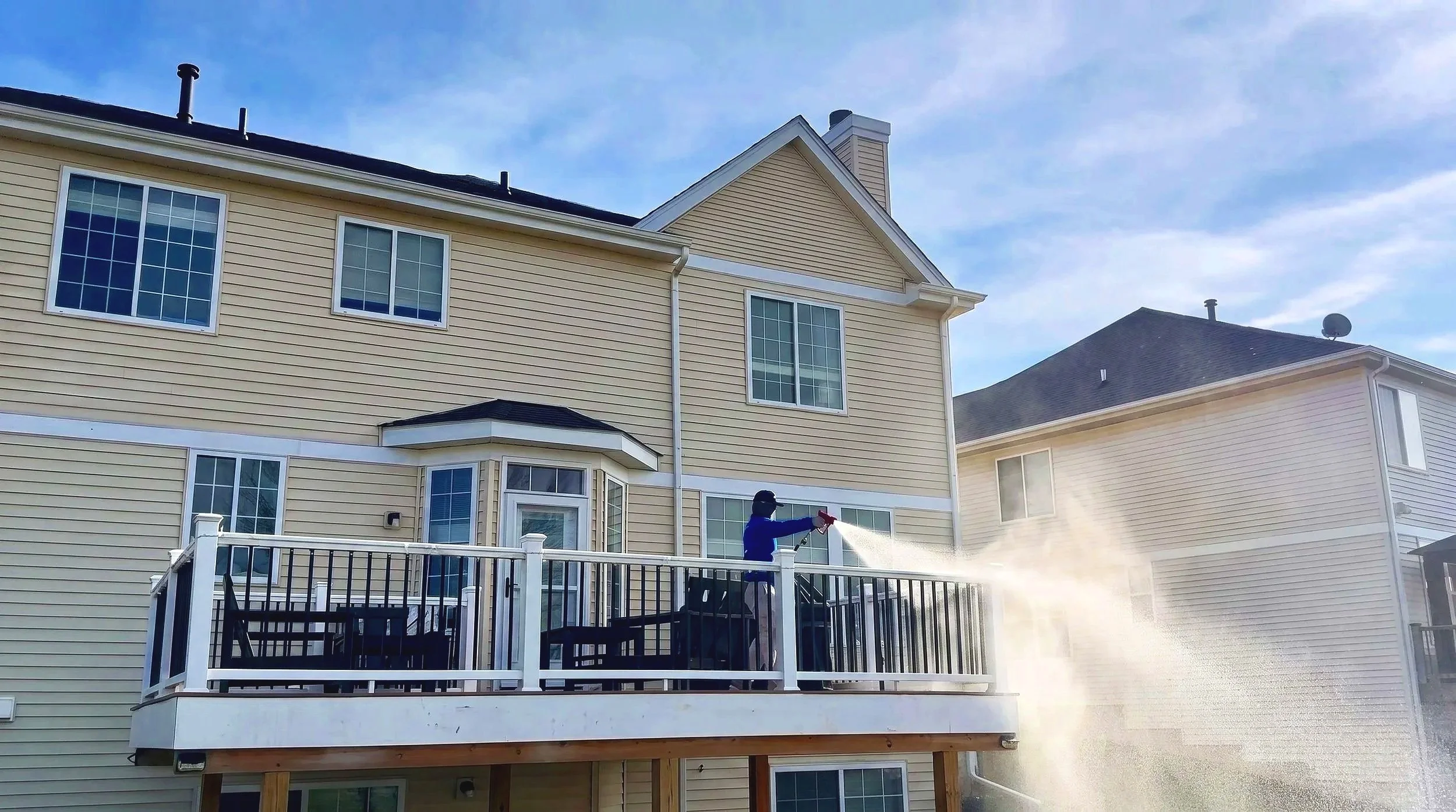Man softwashing deck yellow house face covering