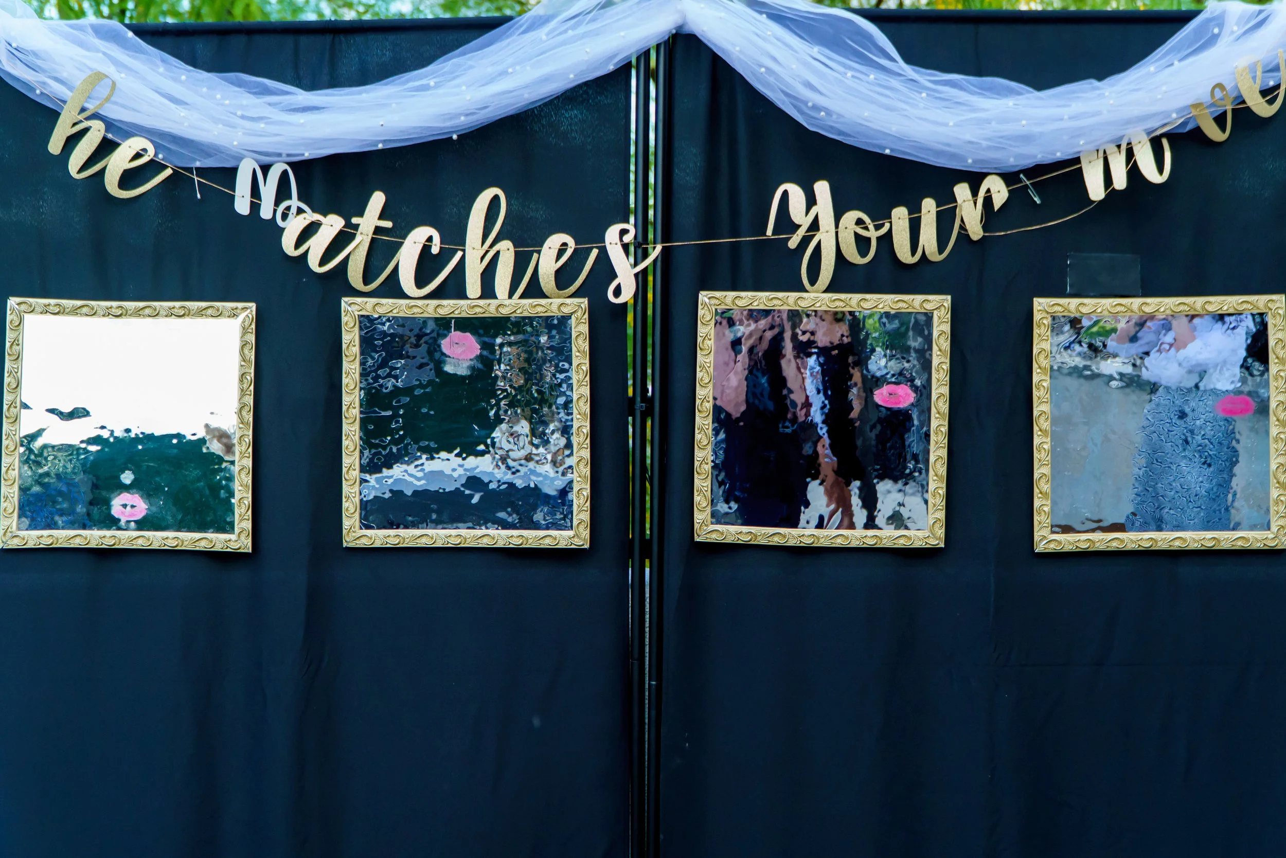 A display board with a gold glittery 'Happy Match' sign, decorated with white tulle fabric at the top and three framed photographs of pink flowers below.