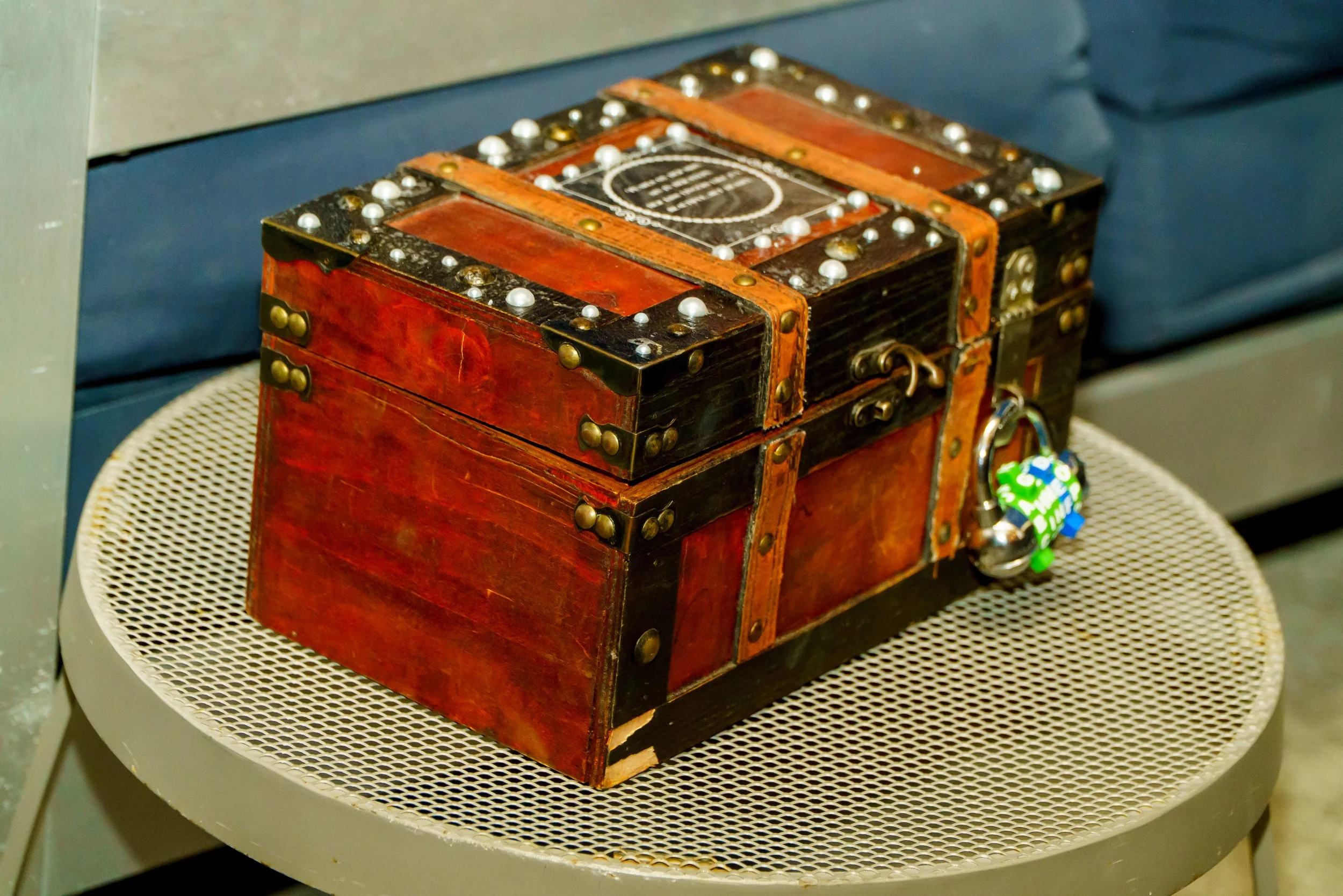 A decorative vintage wooden box with metal studs and leather straps, placed on a white mesh table.