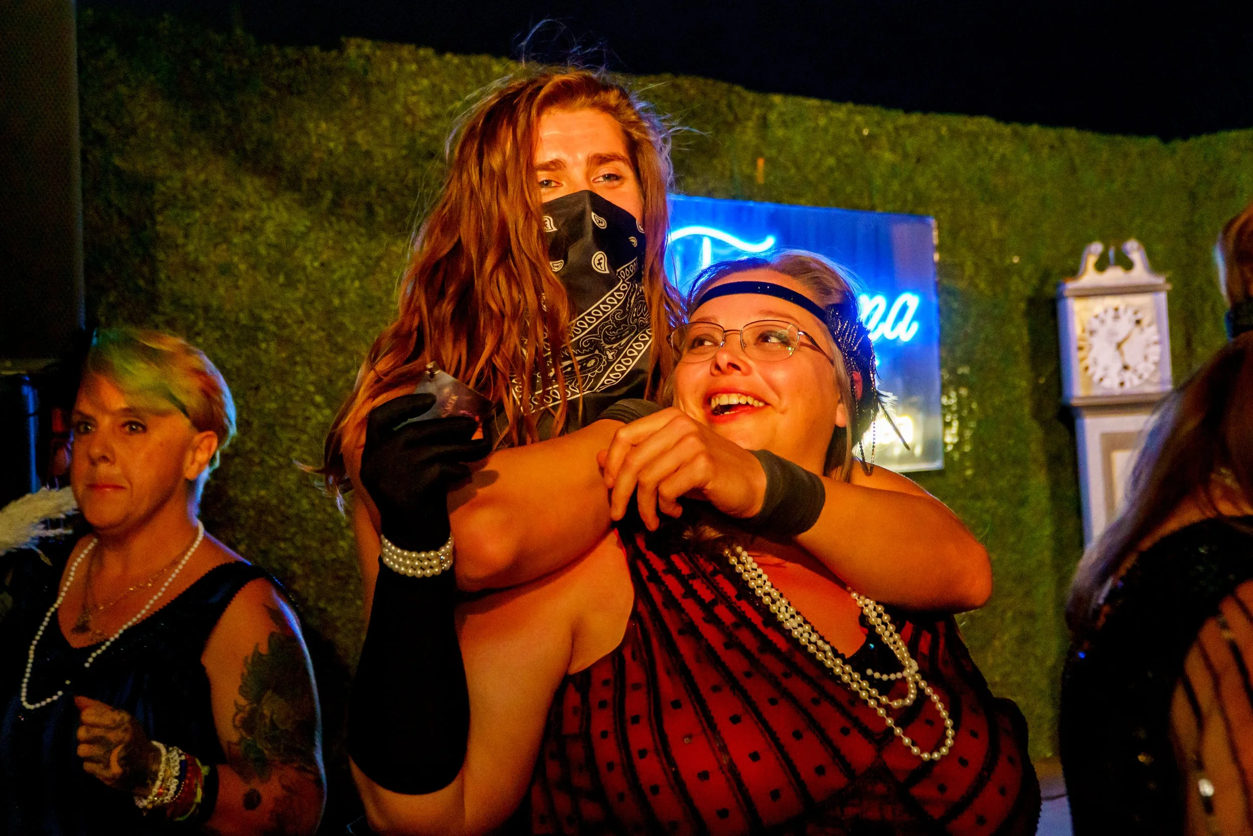 People celebrating at a lively indoor event with festive attire, costumes, and accessories, including pearls, headbands, and masks.