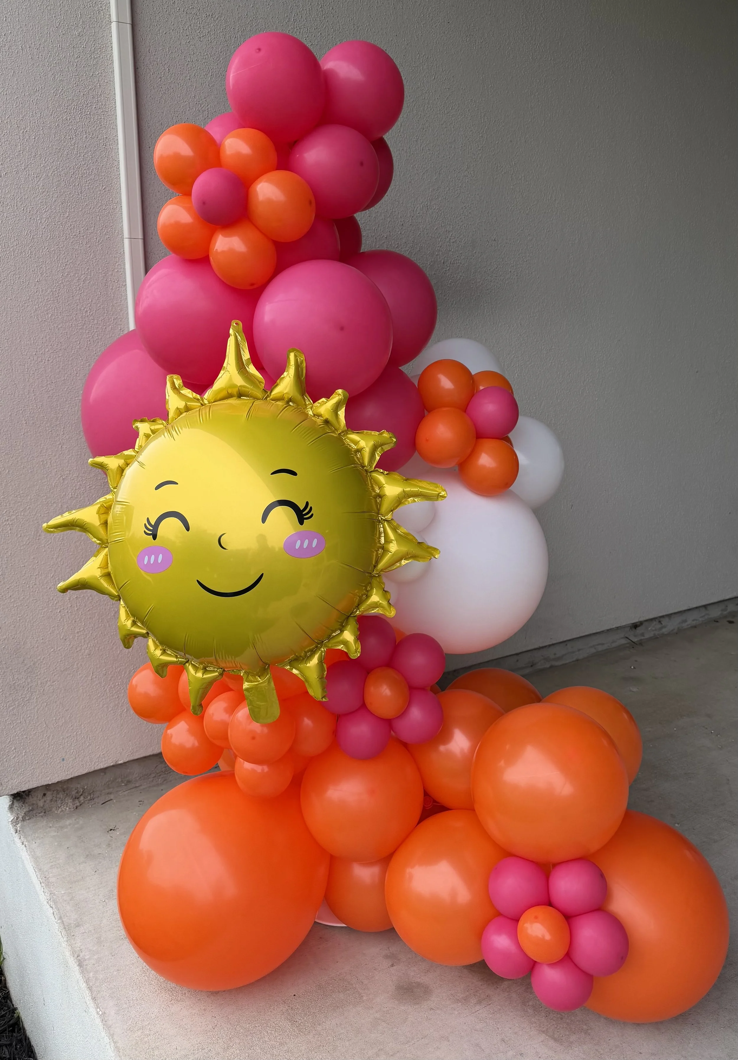 Orange, white and pink balloon decor with an ornamental smiling sun balloon, created by Dripping springs based ColorPop Balloon Studio.