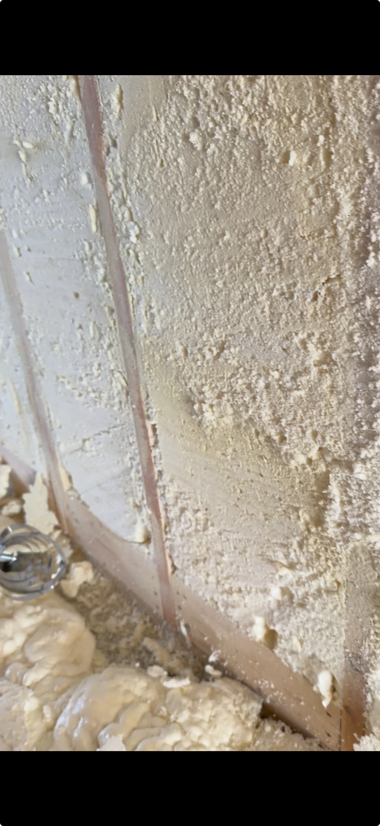 Close-up view of unfinished insulation and drywall installation in a wall with some foam insulation on the floor.