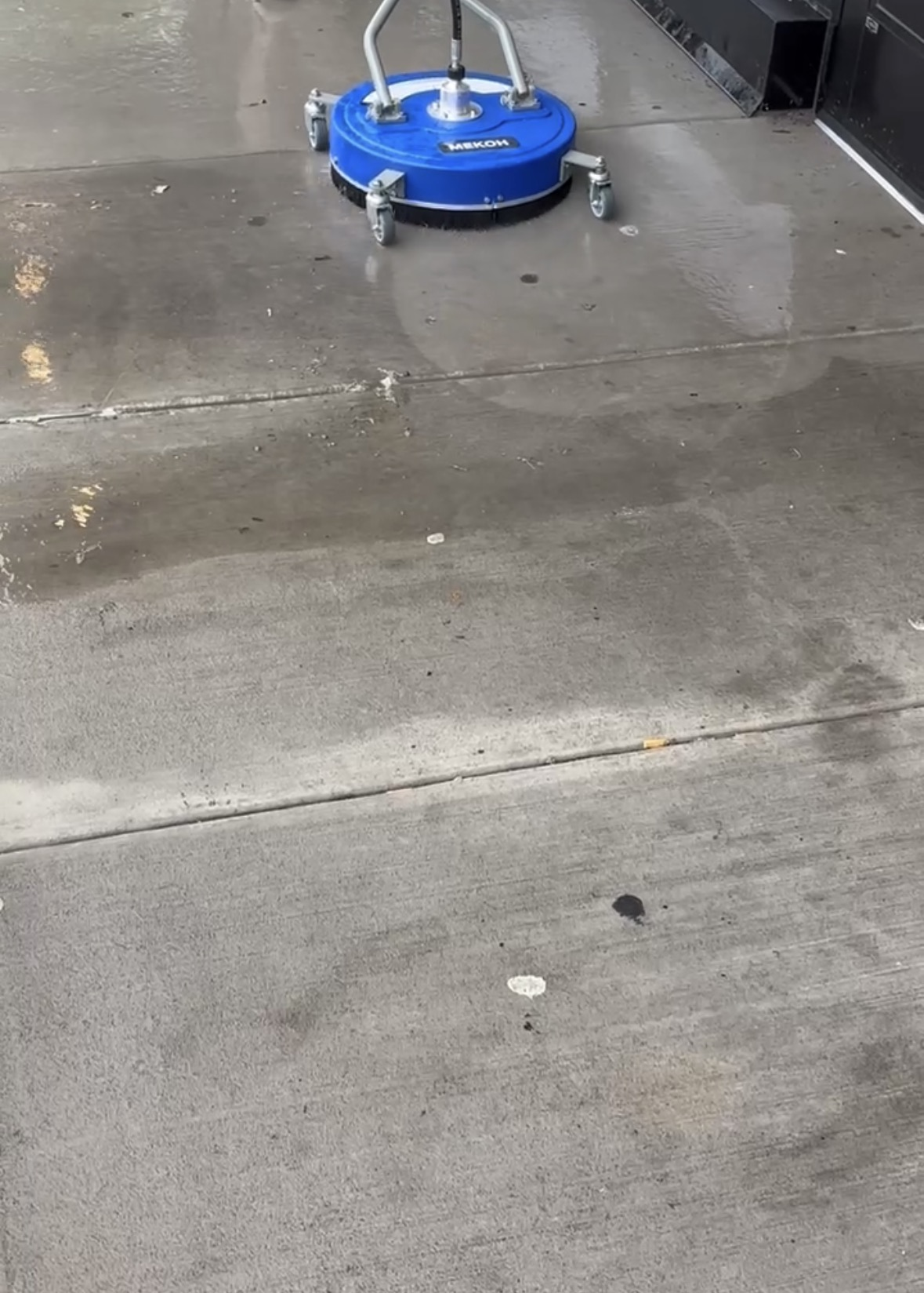A blue floor cleaning machine on a wet concrete surface.