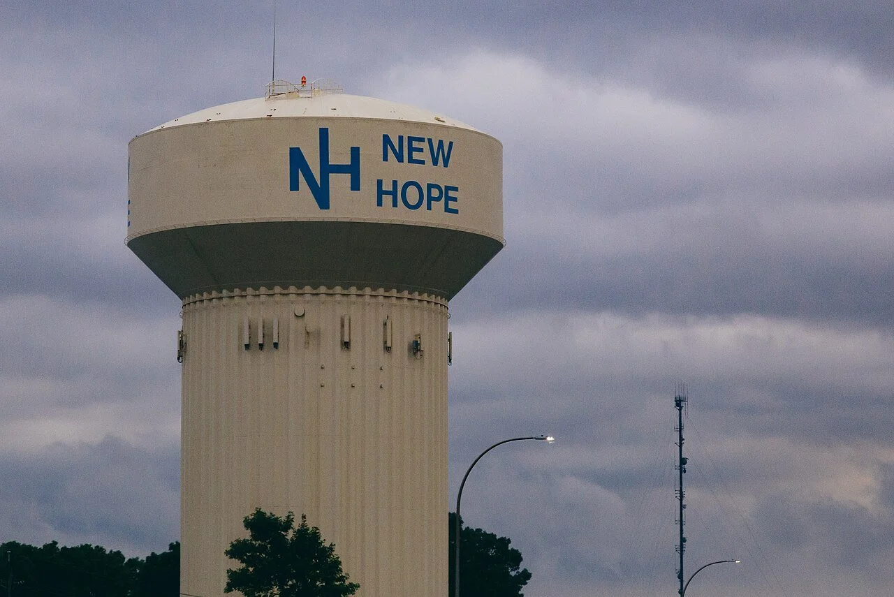 Water tower with the words 'New Hope' and 'NH' painted on it, against a cloudy sky.