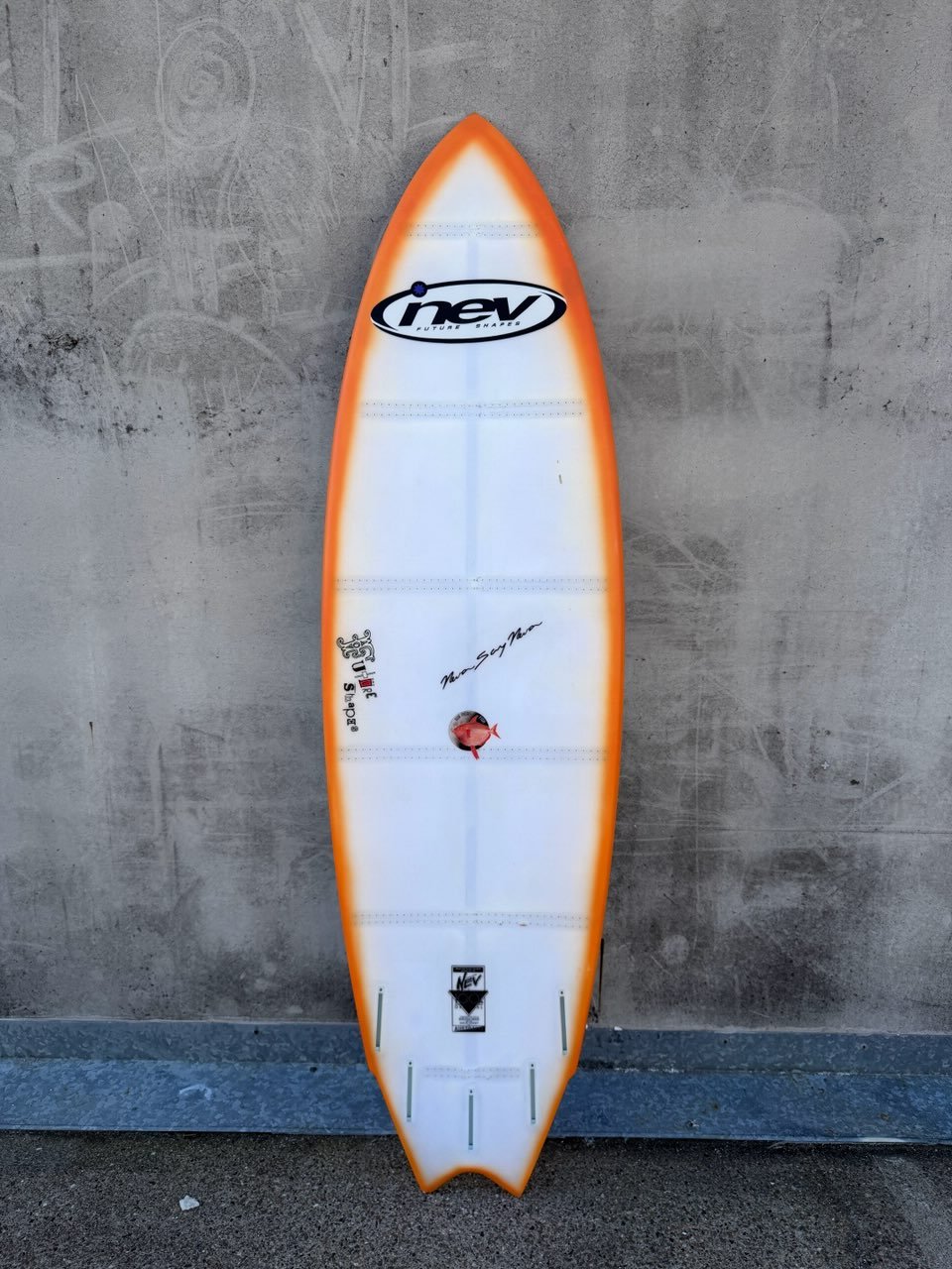 A surfboard with lights in it with various logos and signatures, leaning against a concrete wall.