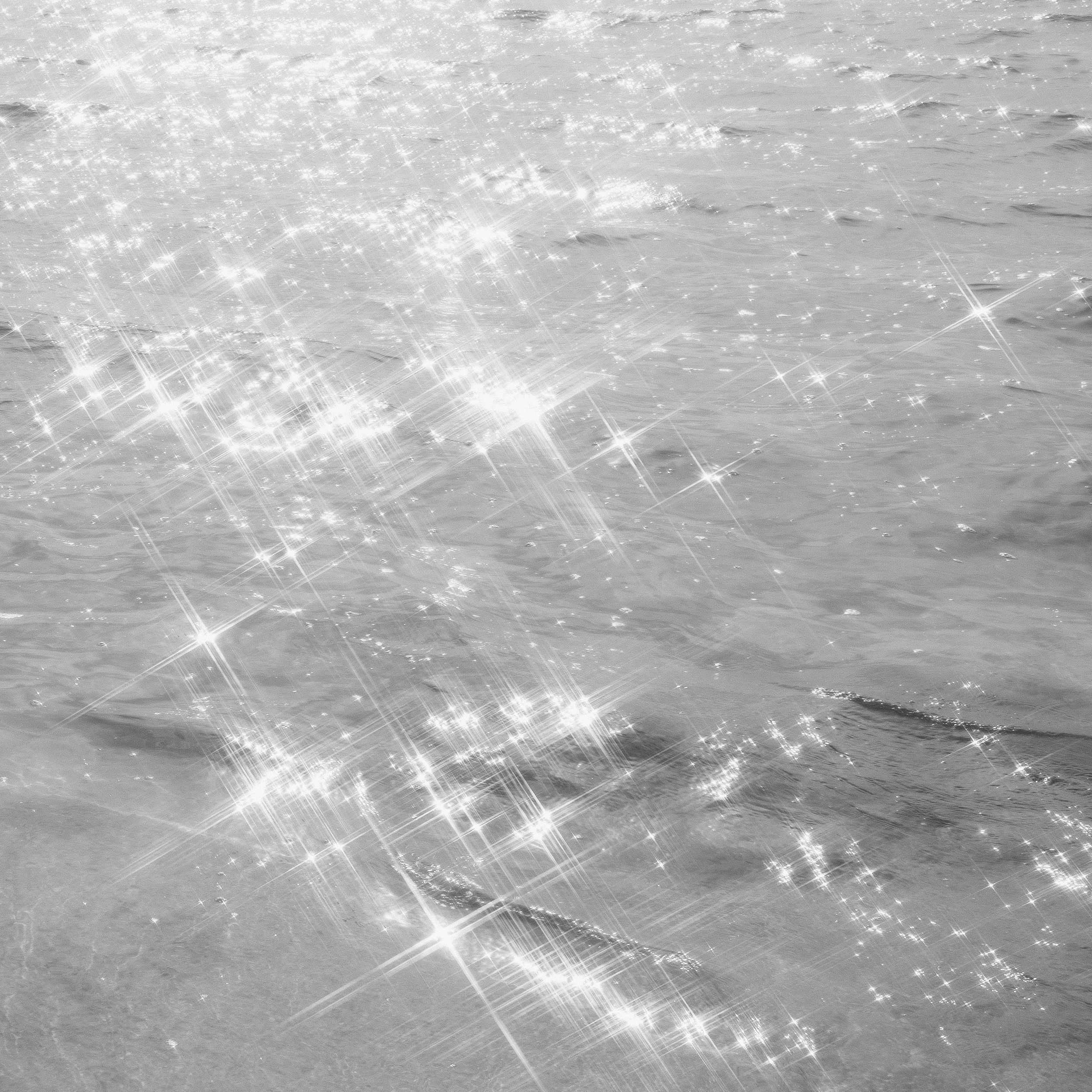 Shiny, glittering water surface with sunlight reflecting, creating sparkles and star-shaped glints.