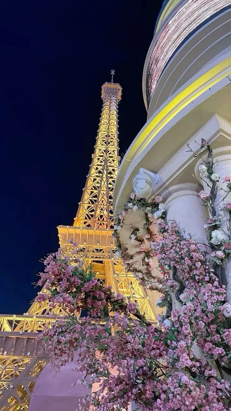 The Eiffel Tower illuminated at night with pink and white flowers in the foreground.