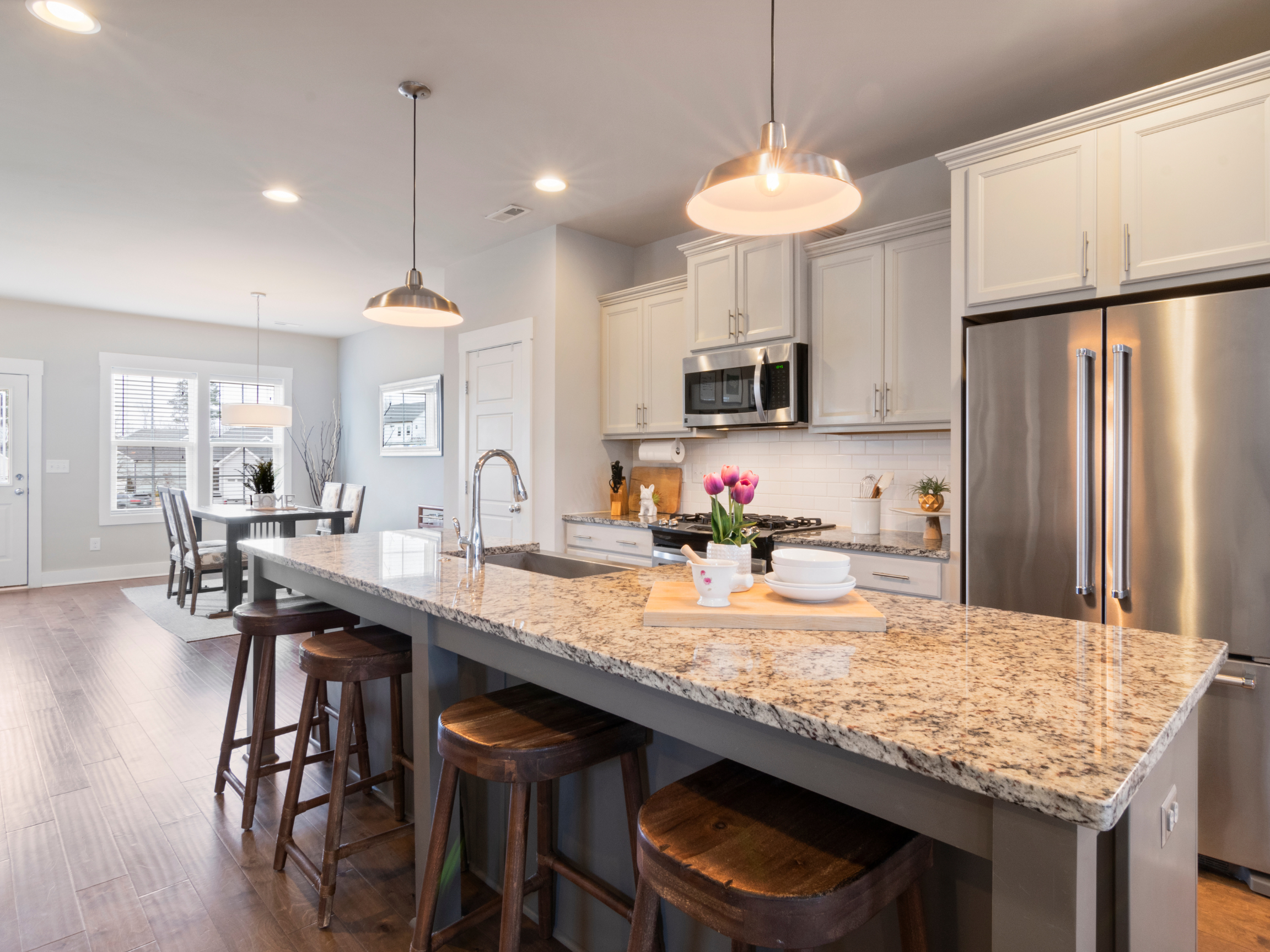 Modern kitchen with granite island, white cabinets, stainless steel fridge, and dining area with wall of windows.