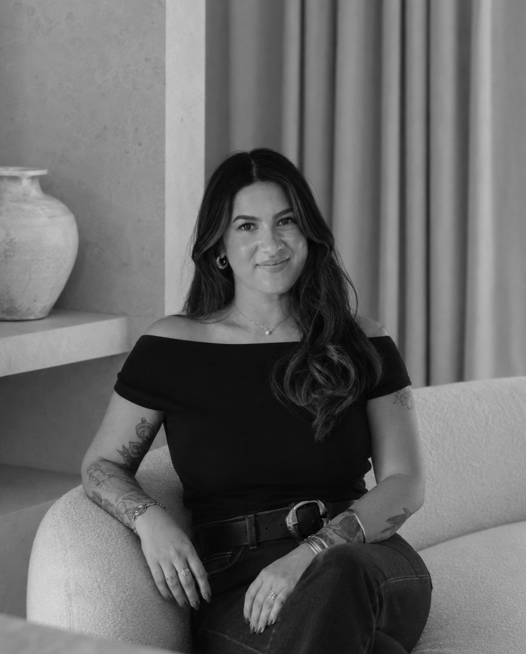 Black and white photo of a woman sitting on a couch in a modern interior, smiling and looking at the camera.