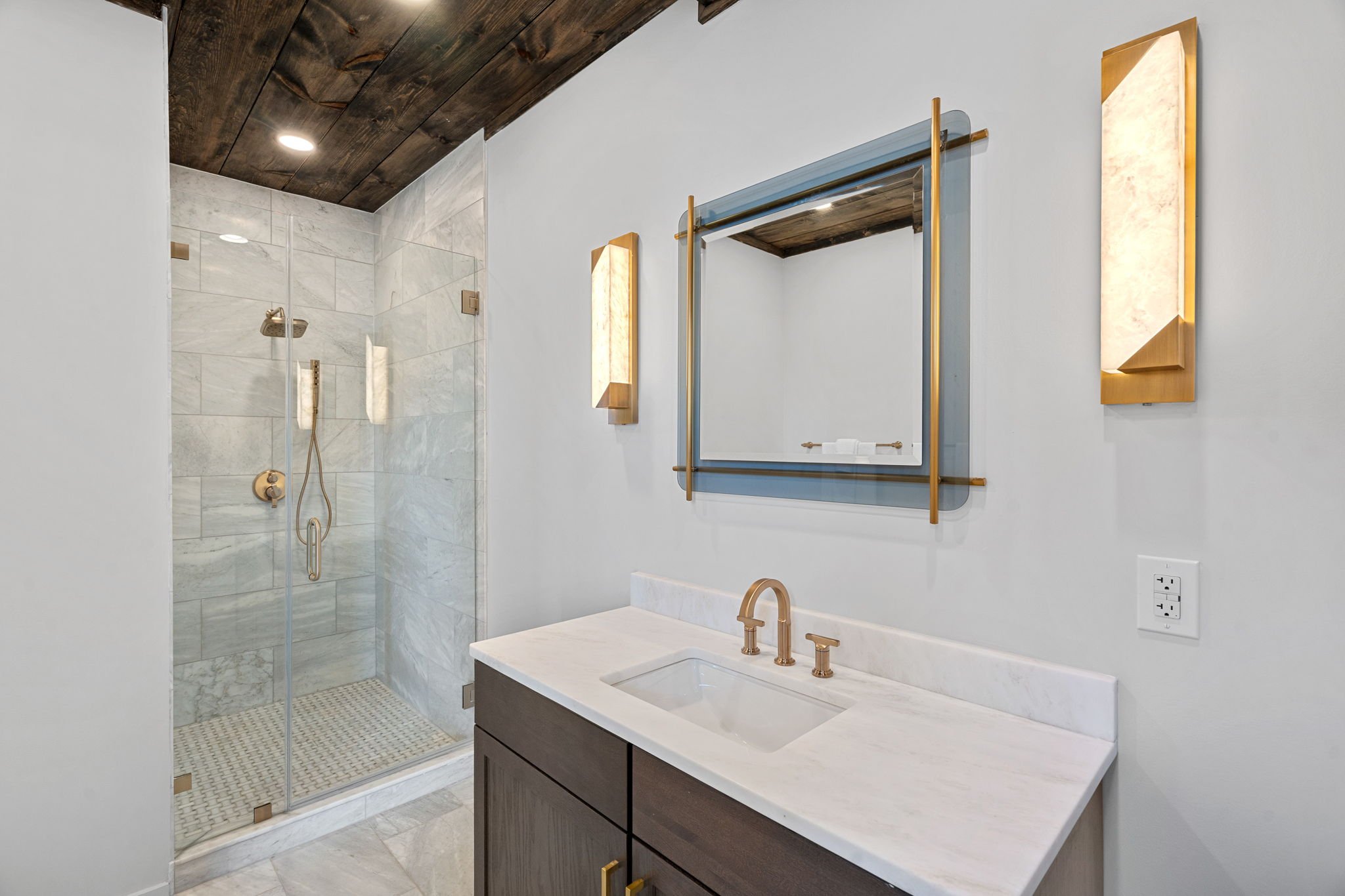 Modern bathroom with a marble shower, a mirror with gold accents, and a white sink with a dark wood vanity.