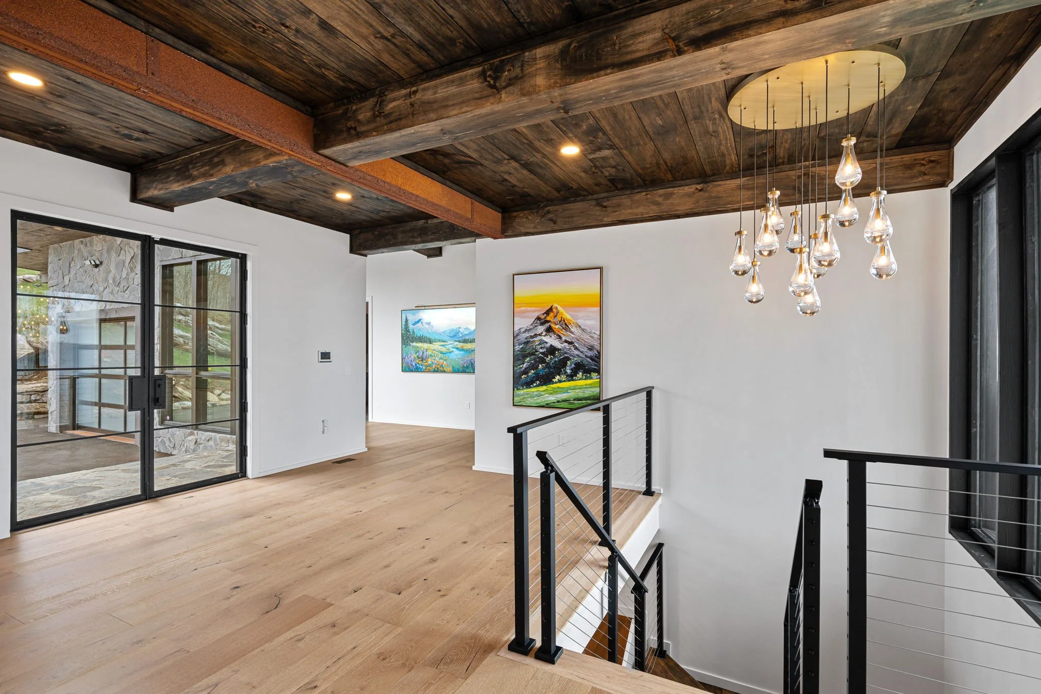 Interior of a modern house with a wooden ceiling, artwork on white walls, and a staircase with black railing.