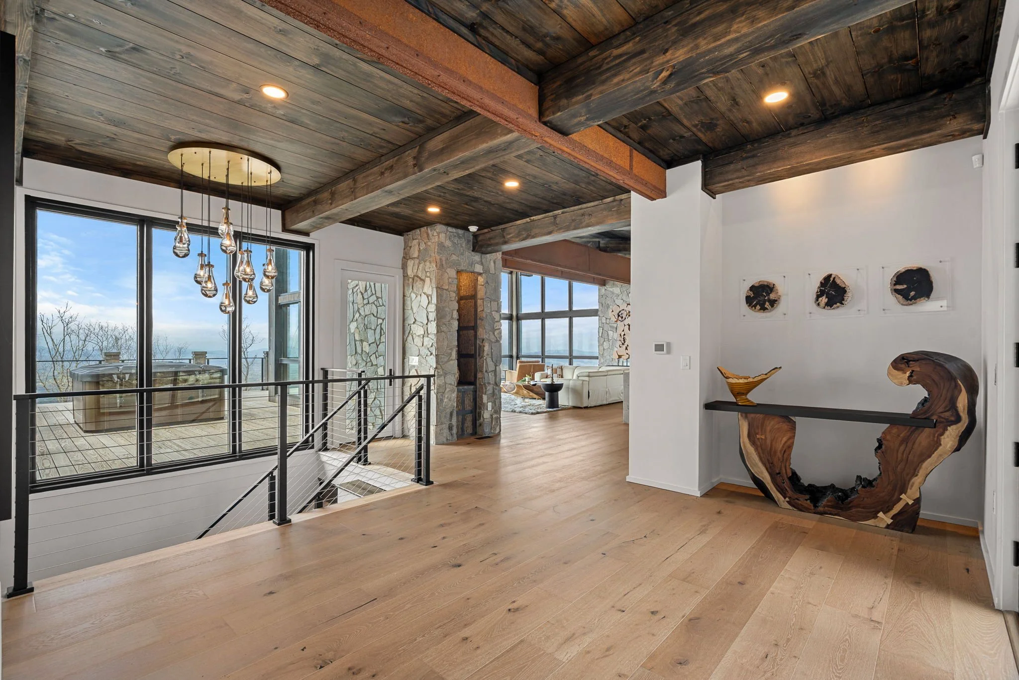 Interior view of a modern home with wood ceiling, stone fireplace, large windows, and contemporary furniture, showcasing a scenic outdoor view.