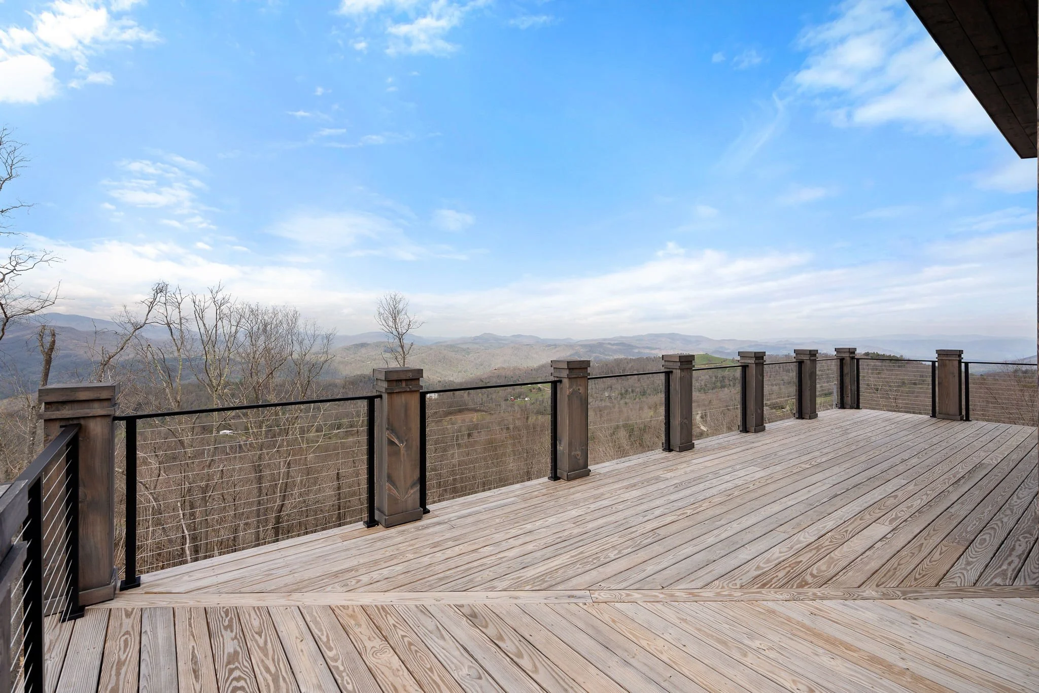 A scenic view from a wooden deck overlooking a mountain landscape with trees and a partly cloudy sky.