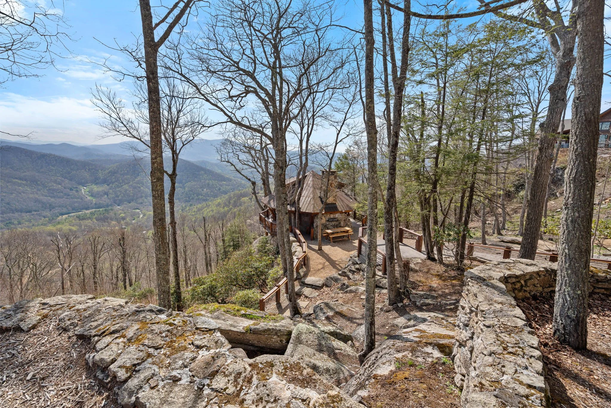 A mountainous landscape with leafless trees, a wooden cabin with a sloped roof, and a clear blue sky.