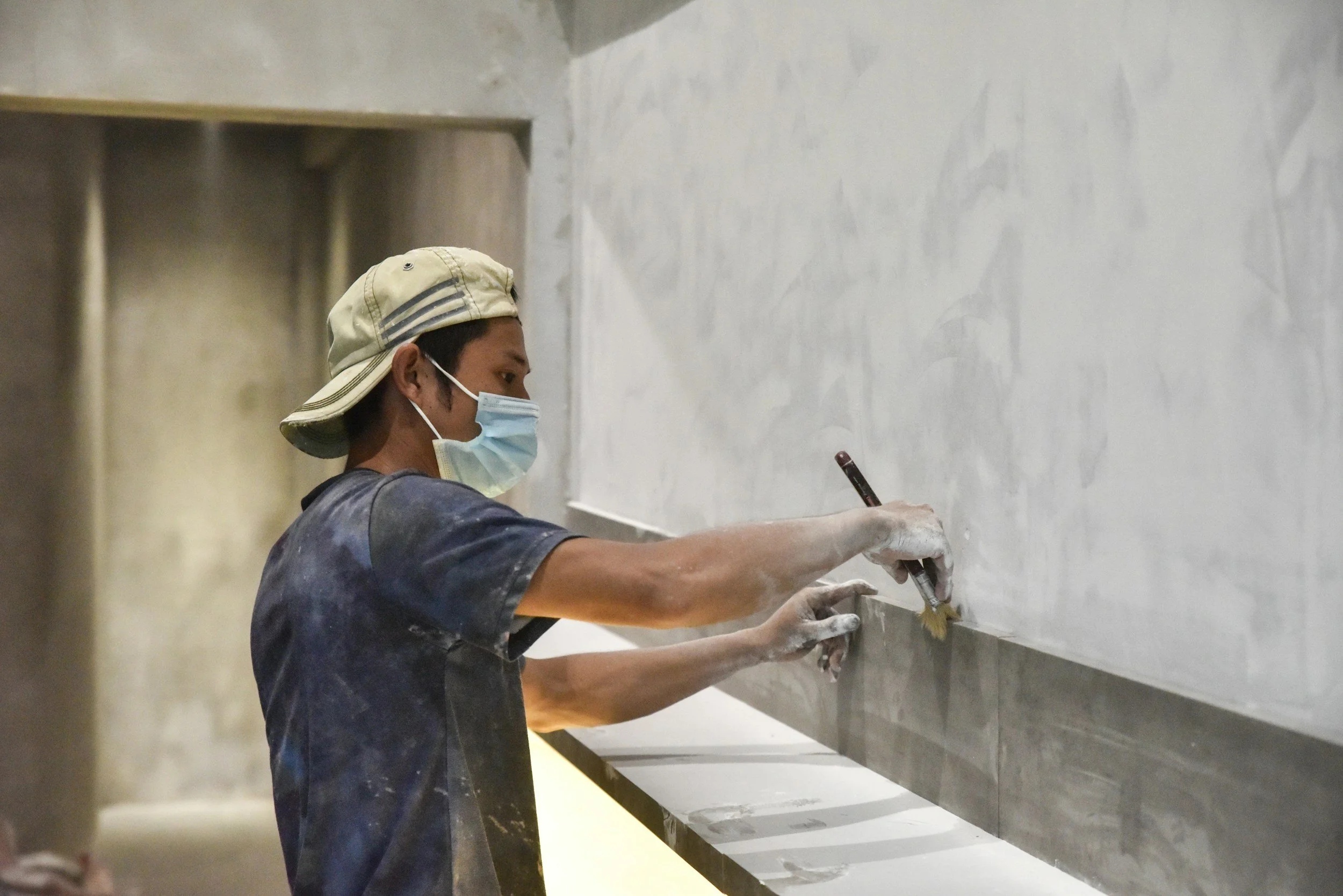 A person wearing a hat and a face mask is polishing a large stone countertop with a polishing tool.