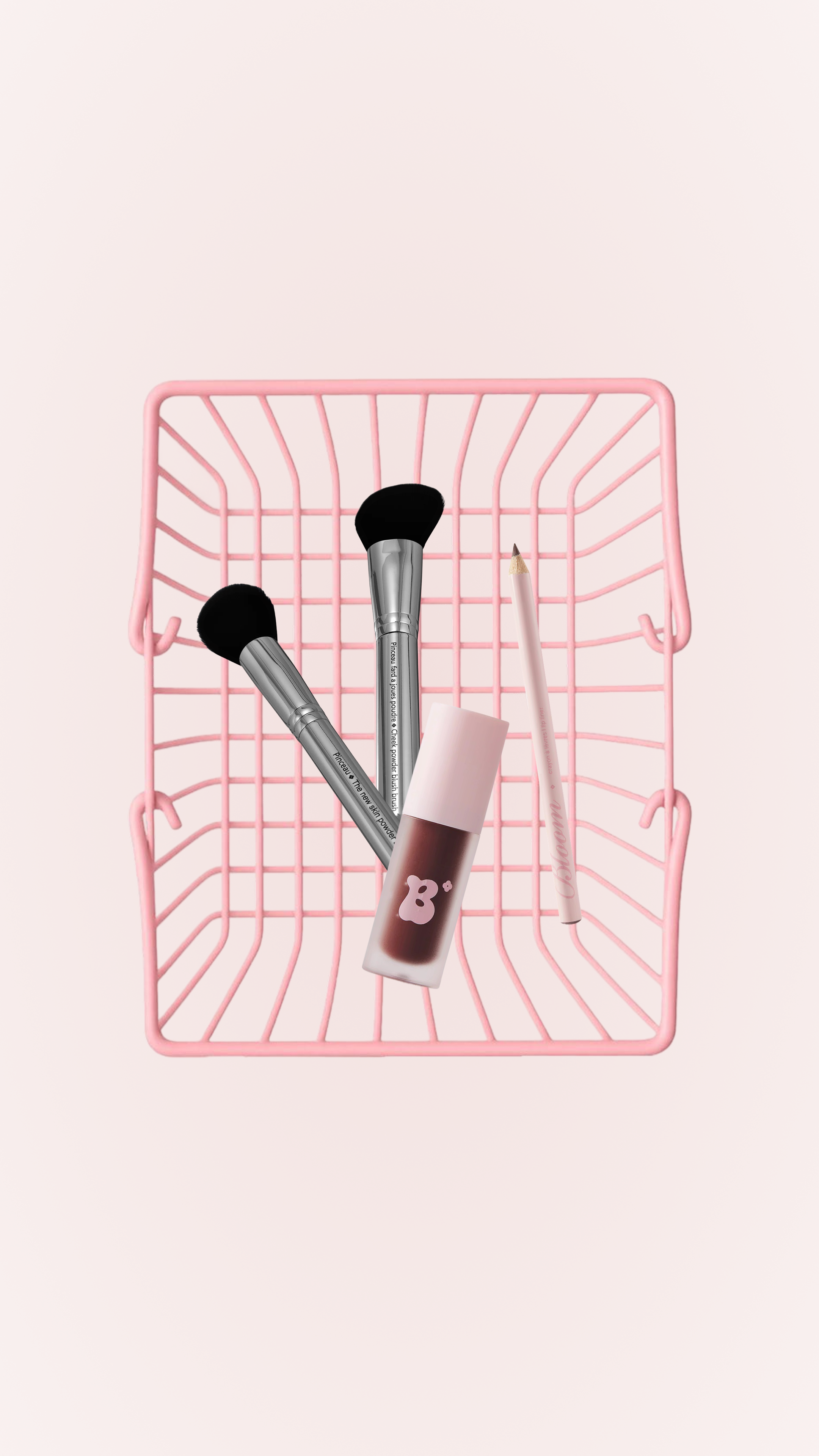 Pink wire basket with makeup brushes, a lip gloss, and a lip pencil inside on a light pink background.
