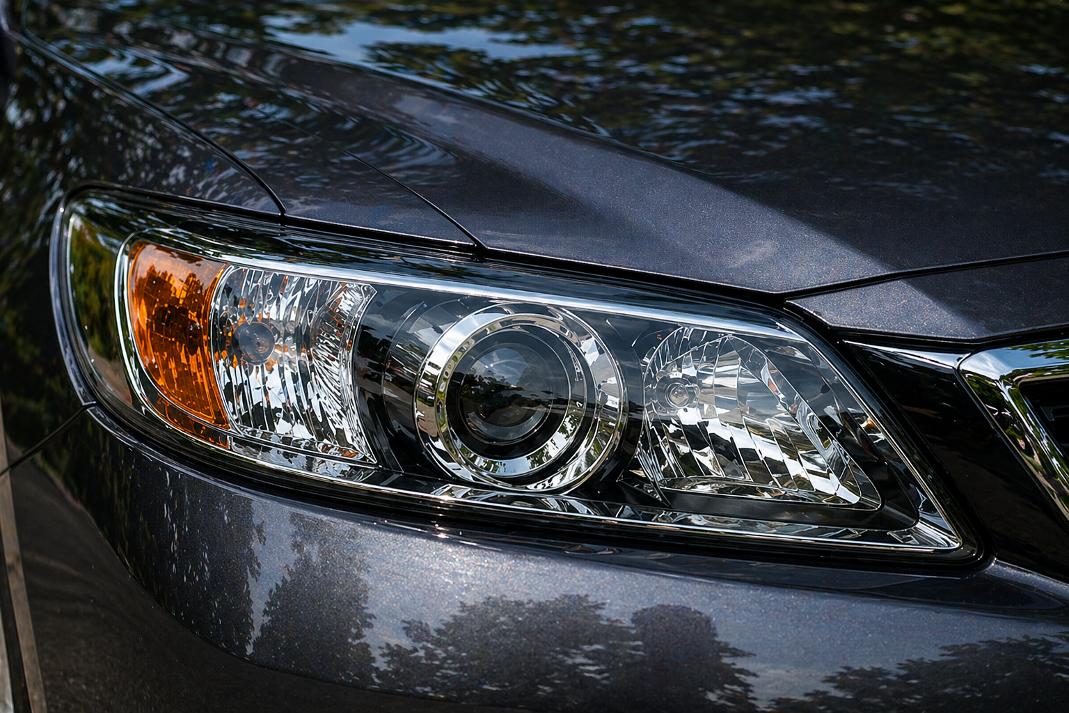 Close-up of a car's headlight with reflections of trees and sky on its surface.