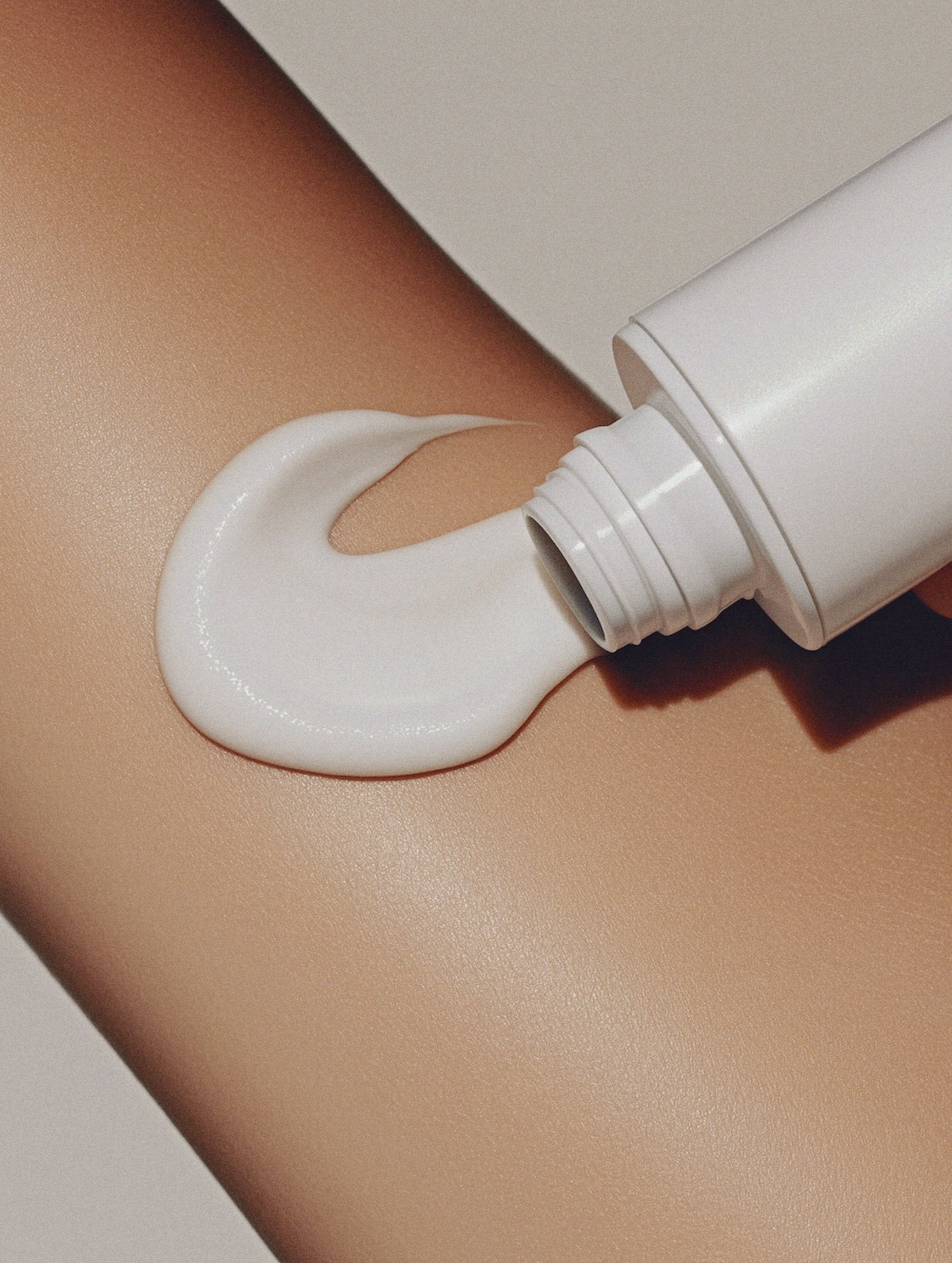 A tube of white lotion squeezed onto a person's skin.