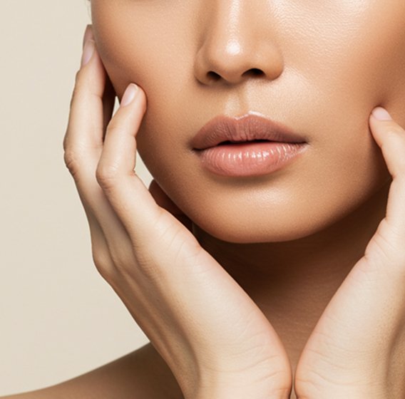 Close-up of a woman’s lips and chin with her hands gently touching her face.