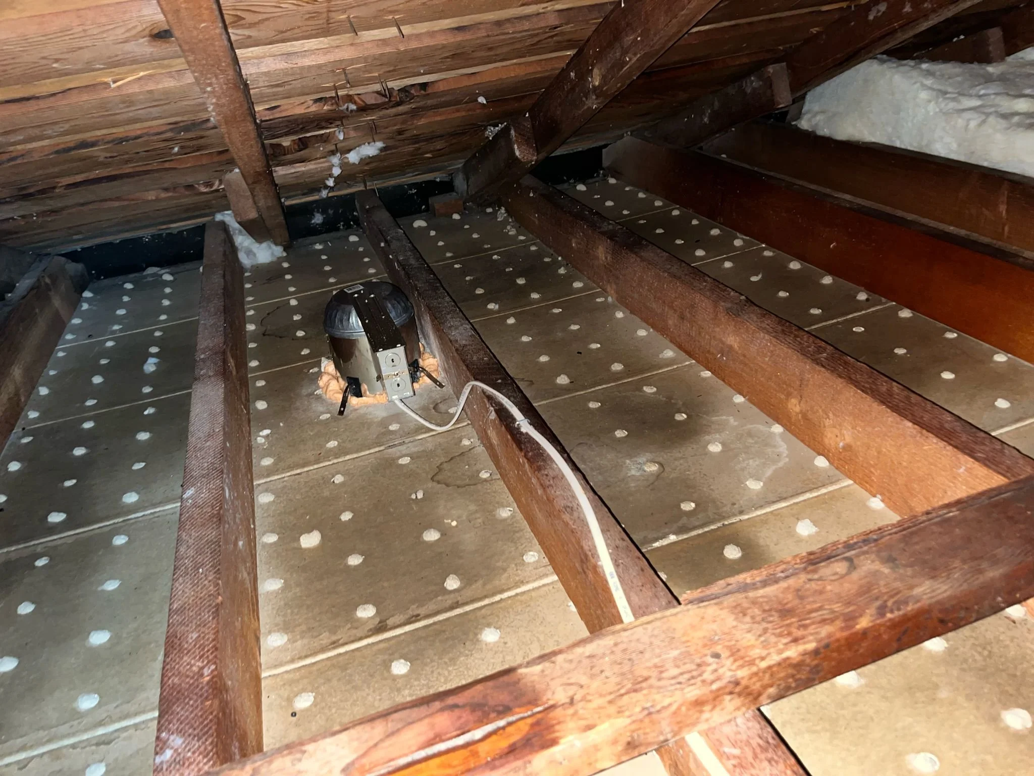 Attic with wooden framing, spray foam insulation on the walls, and a small canister vacuum cleaner plugged in.