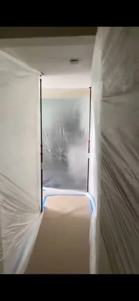 Hallway with plastic sheeting covering the walls and doorways, likely for renovation or painting.