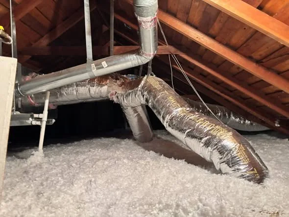 Insulation and ductwork in an attic space with wooden roofing supports.
