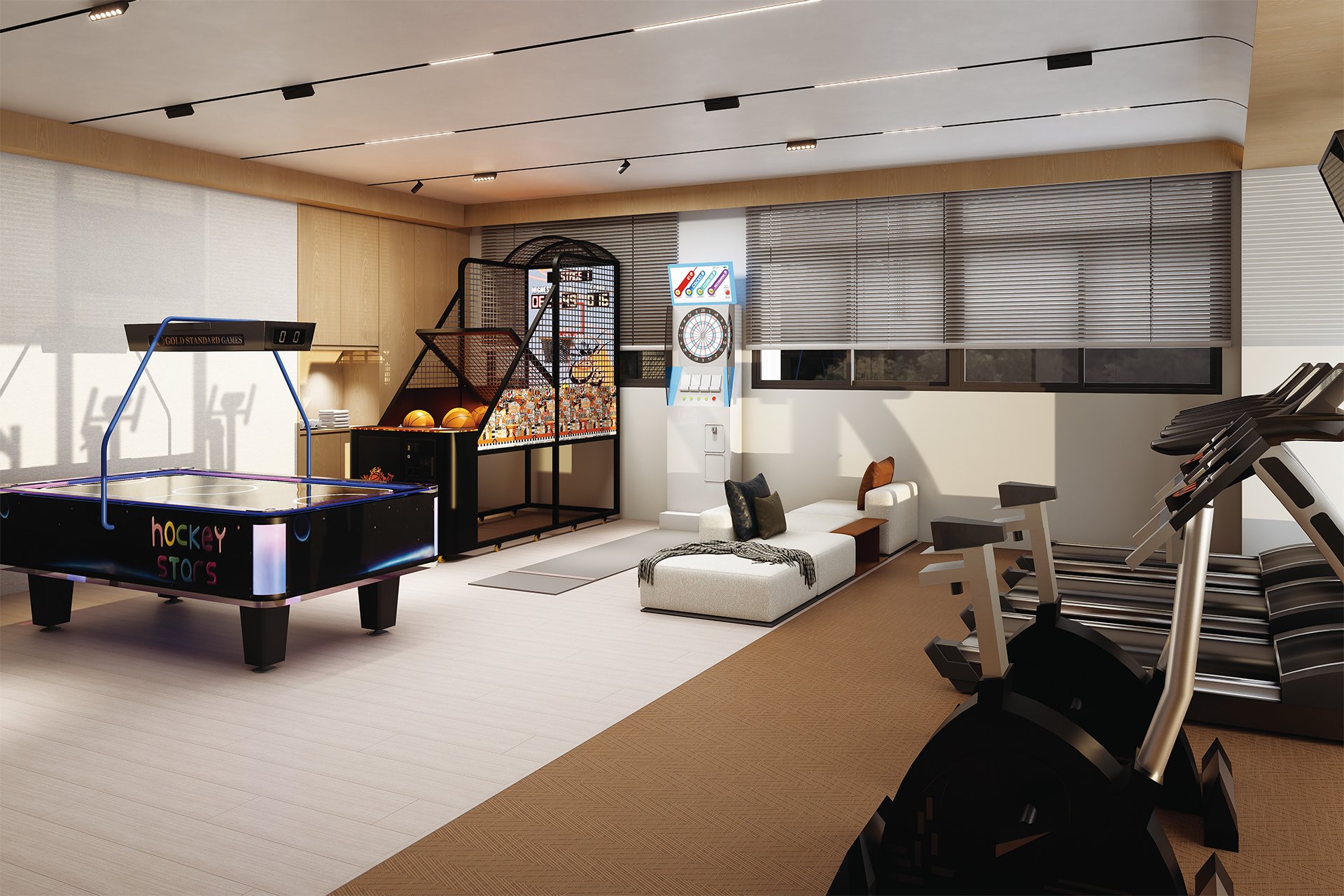 Indoor recreational and fitness area with a hockey table, arcade basketball game, dartboard, and dartboard machine. There are chairs, a small sofa, and exercise bikes near large windows with blinds.