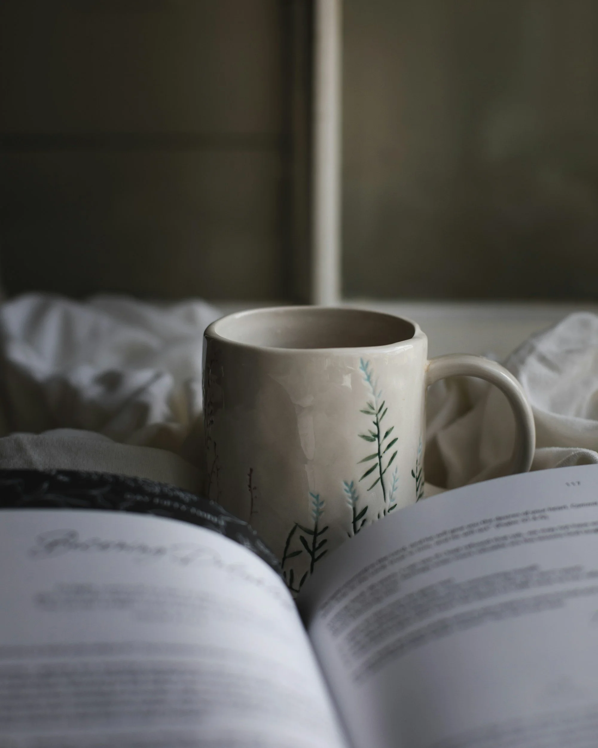 A mug and an open book are lying on a bed