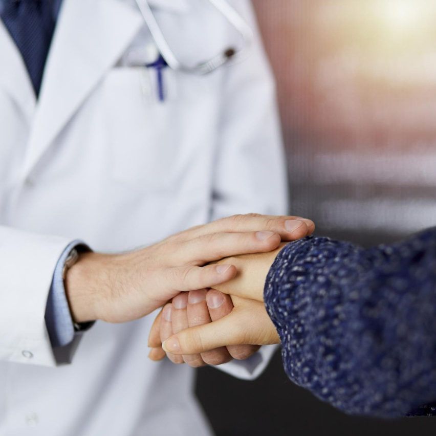 Doctor in white coat holding and examining a patient's hand.