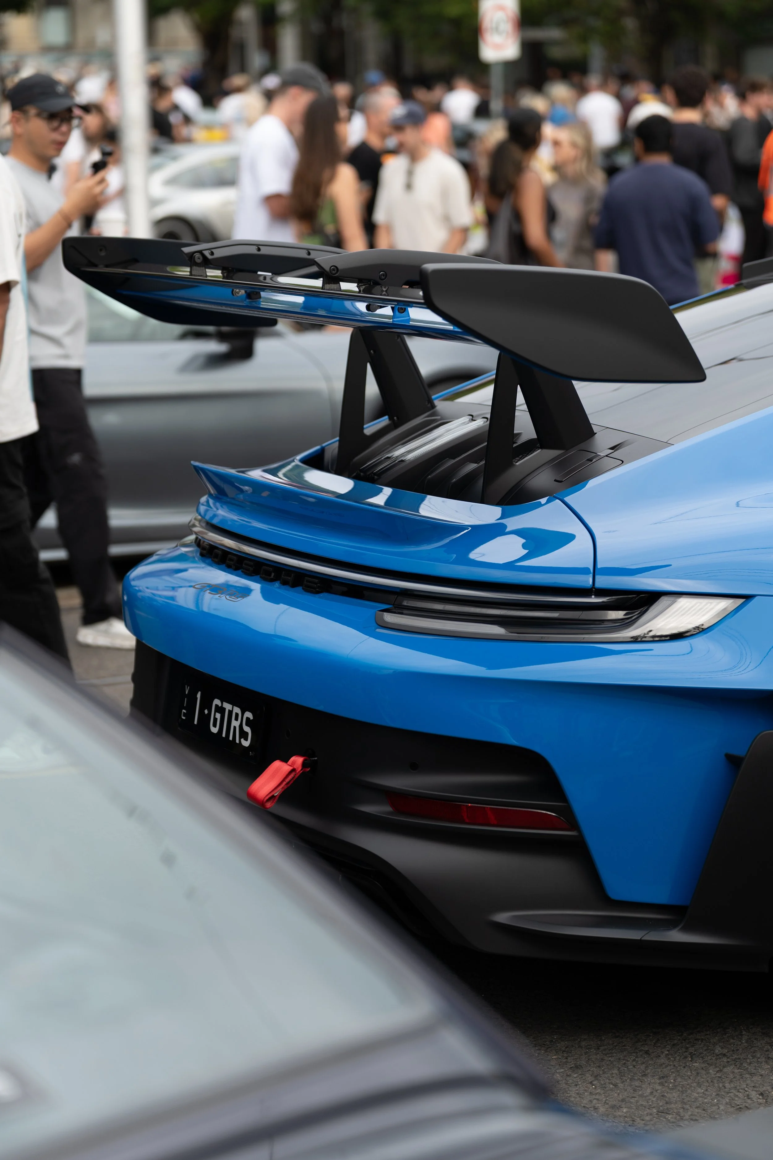 Close-up of a blue sports car porsche 911 gt3 rs race car with a prominent rear wing, parked among a crowd of people during an outdoor event. melbourne porsche coffee meet 2026