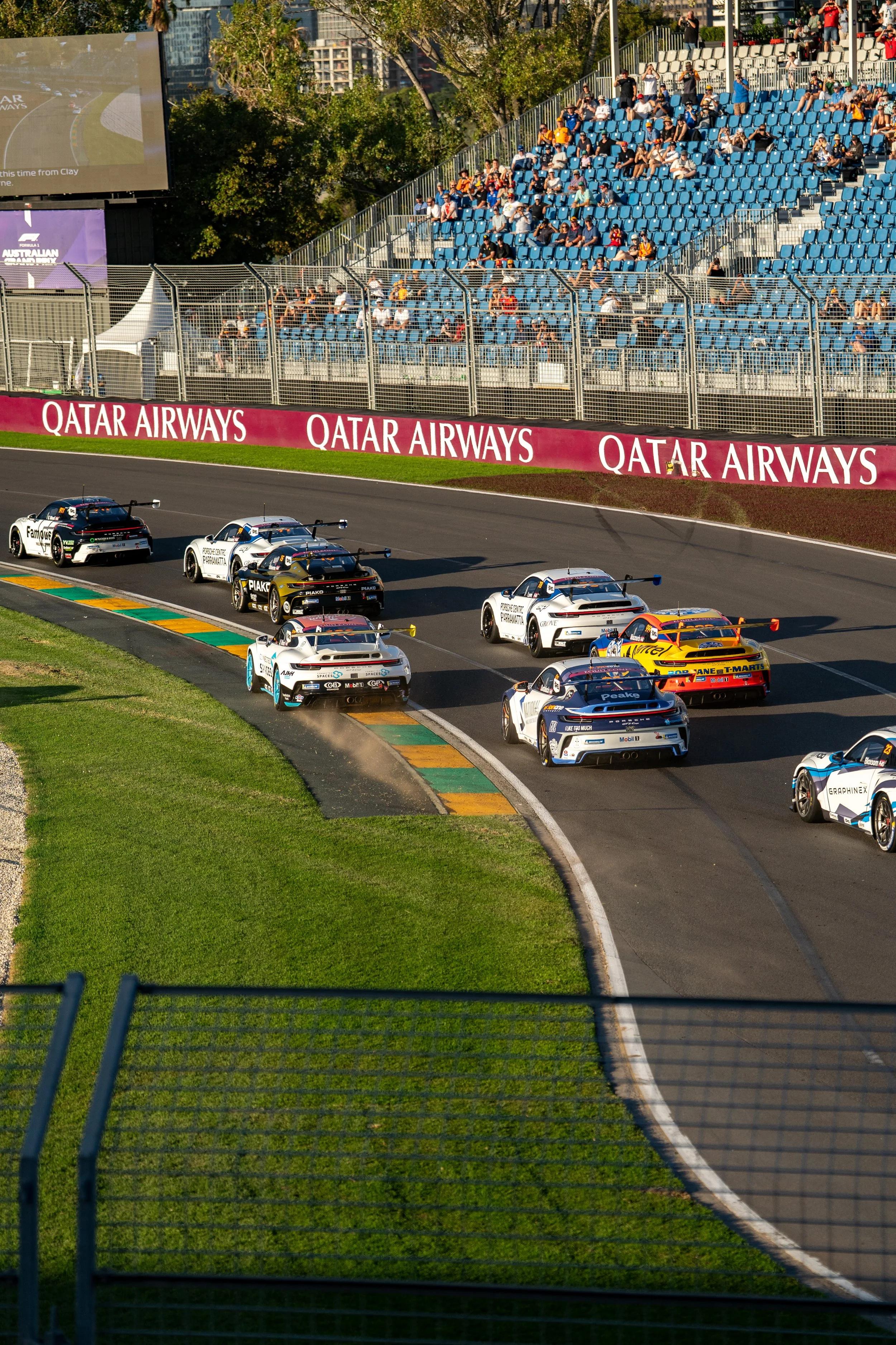 Race cars on track at a motorsport event with spectators in the stands and trees in the background. Porsche 911 gt3 Carrera Cup Australian Grand Prix 2026
