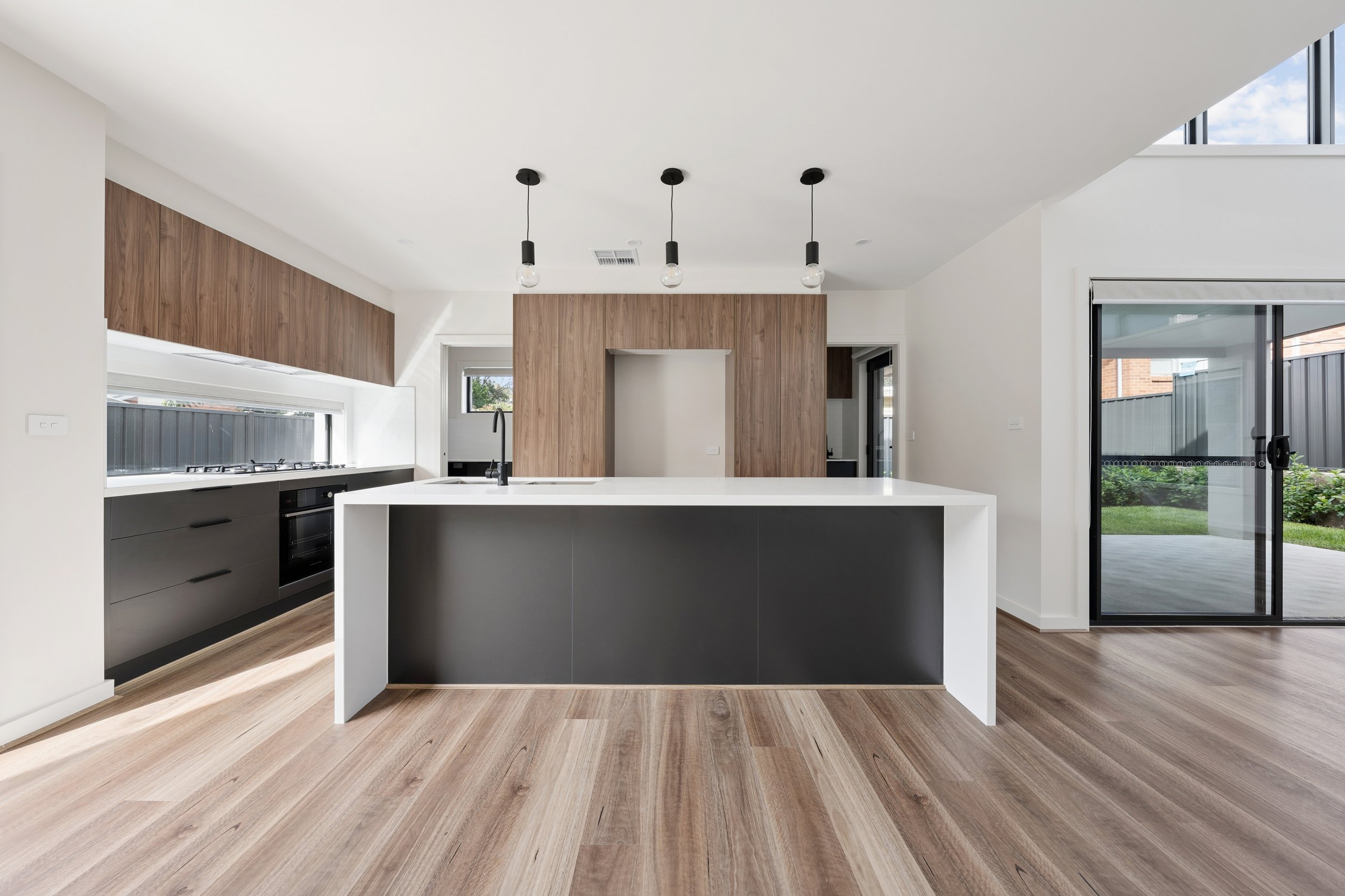 Modern kitchen with white island, black lower cabinets, wood accent walls, and large sliding glass doors leading outside. new build real estate sales photography in Lyons 