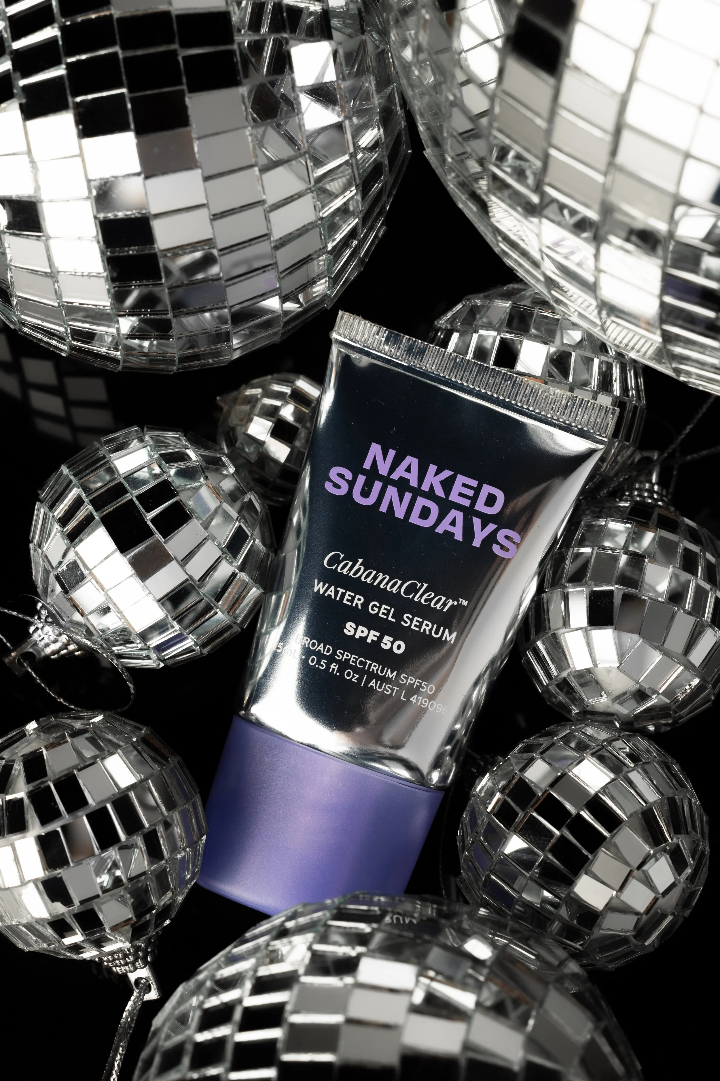 A tube of Cabanaclear water gel serum with SPF 50 surrounded by reflective, mirrored disco balls. naked sundays sunscreen 