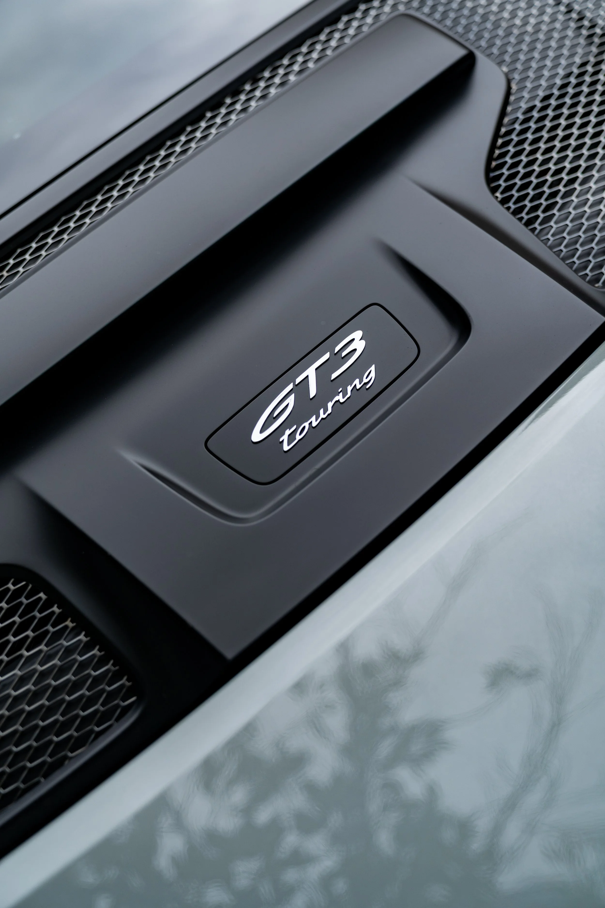 Close-up of a black car's front grille with a badge that reads 'GT3 Touring'. Porsche 911 