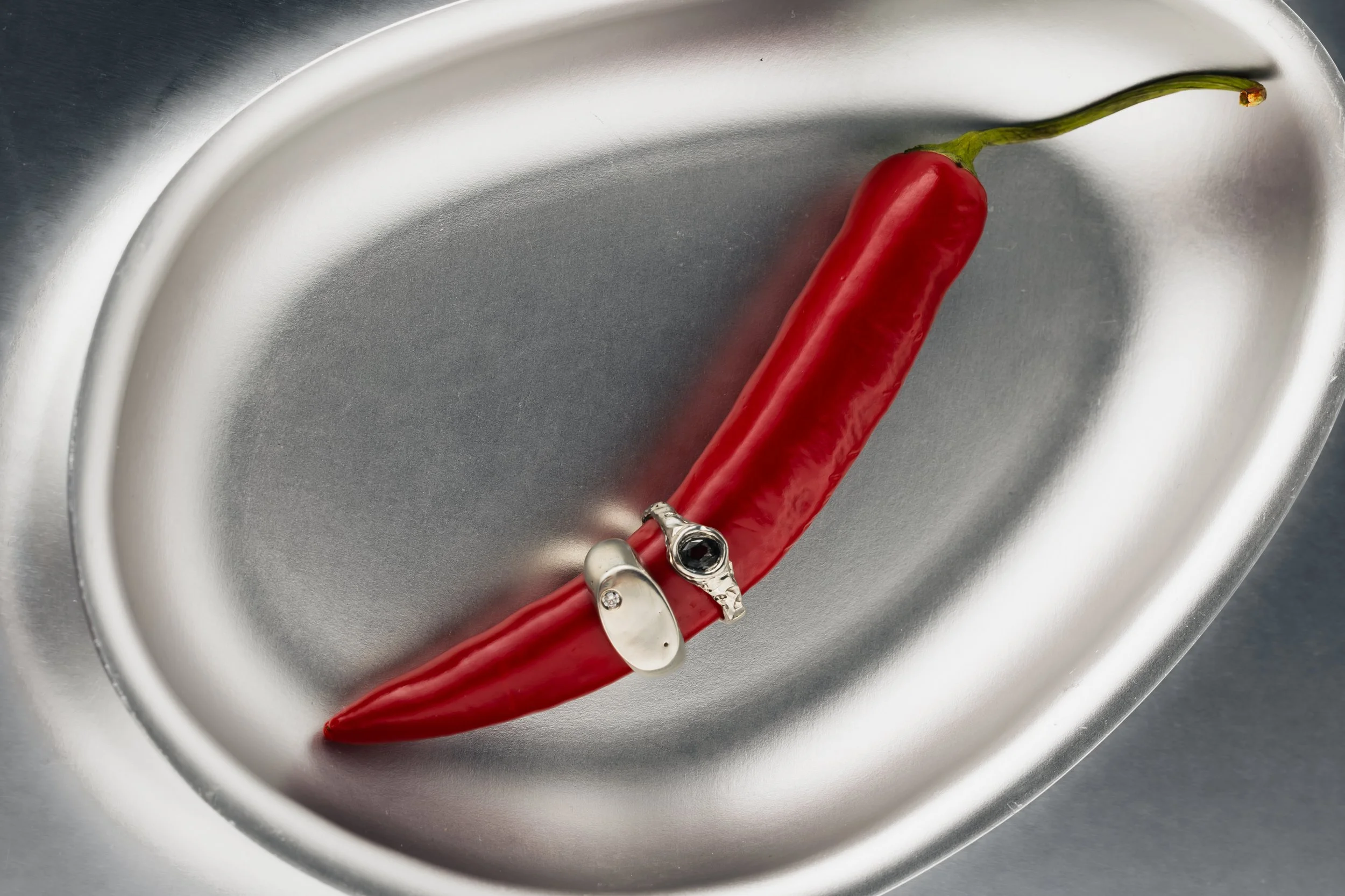 A red chili pepper with a green stem in a silver metallic sink or basin. Fink dish with  jewellery product photography