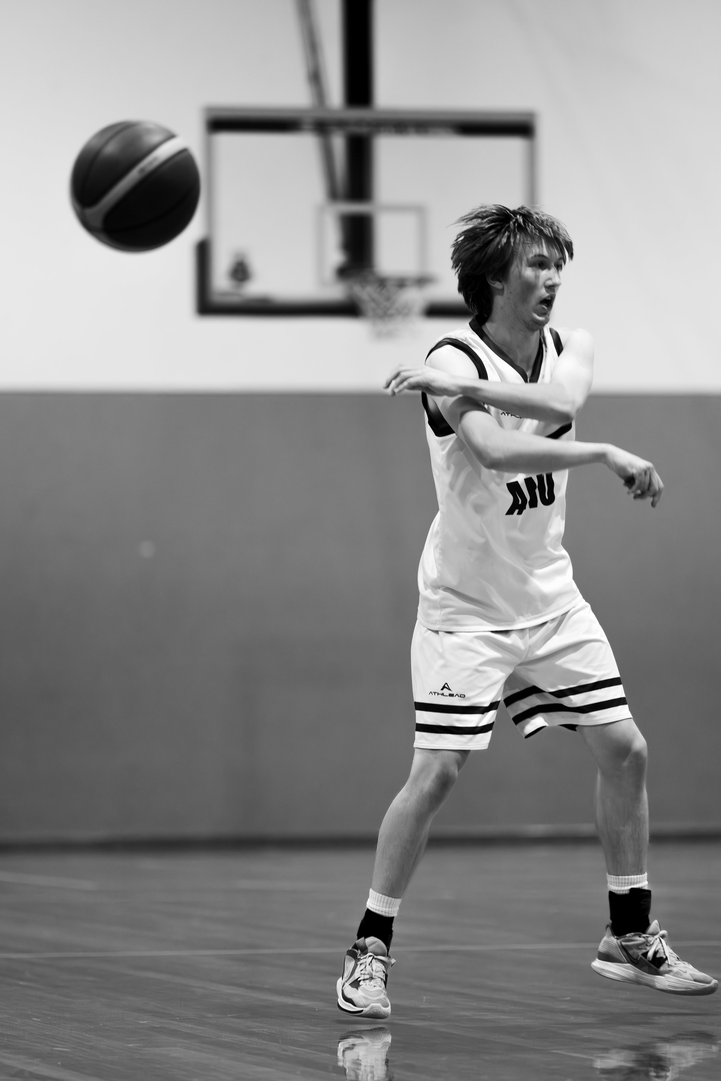 A black and white photo of a male basketball player in a gym, playing basketball. ANU australian national university basketball mens team sports photography