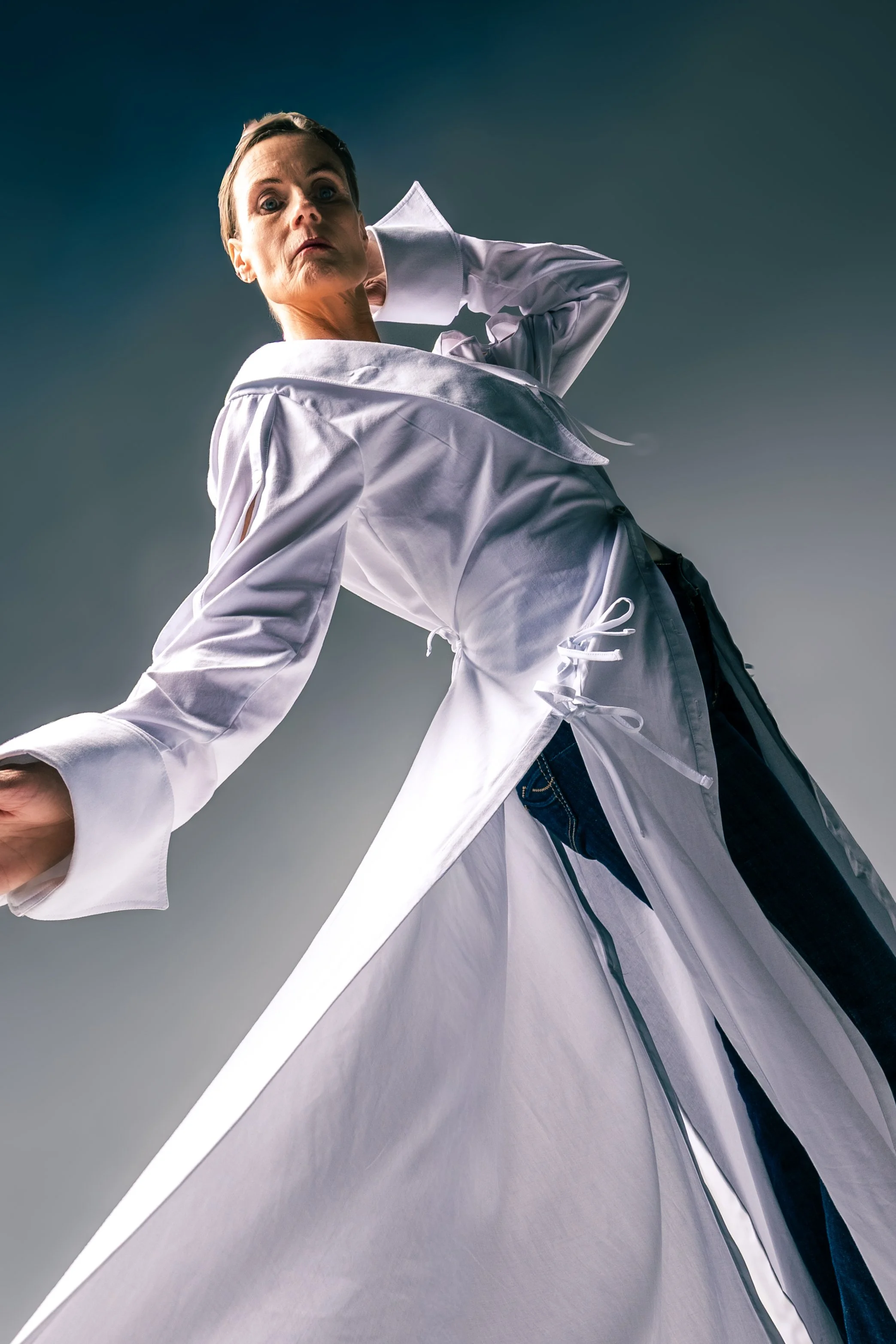 Woman in white chef coat leaning backward with a surprised or curious expression, dark background.