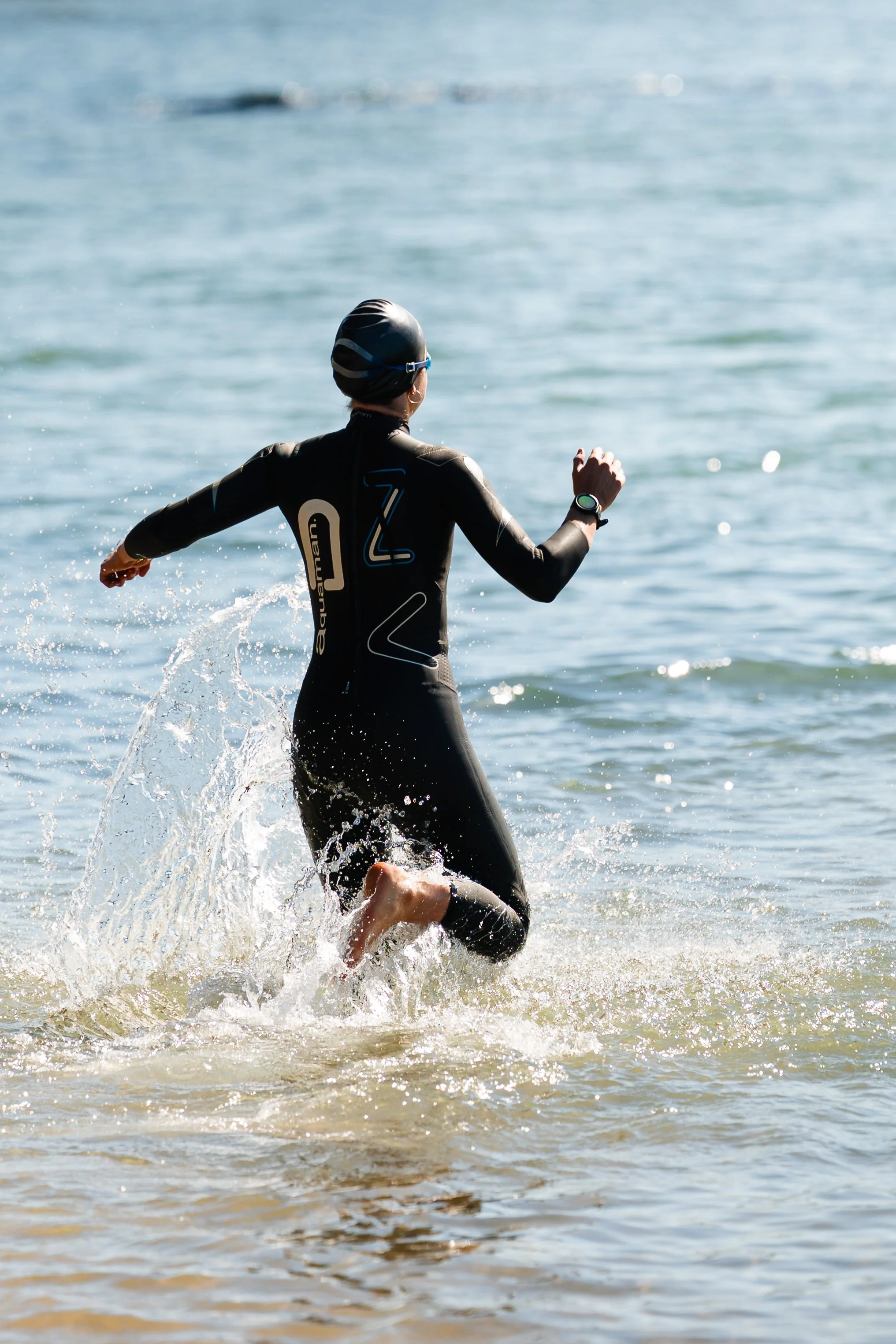 A person wearing a wetsuit and swim cap running out of the water at the beach. Wollongong Triathlon 2026 sports photography