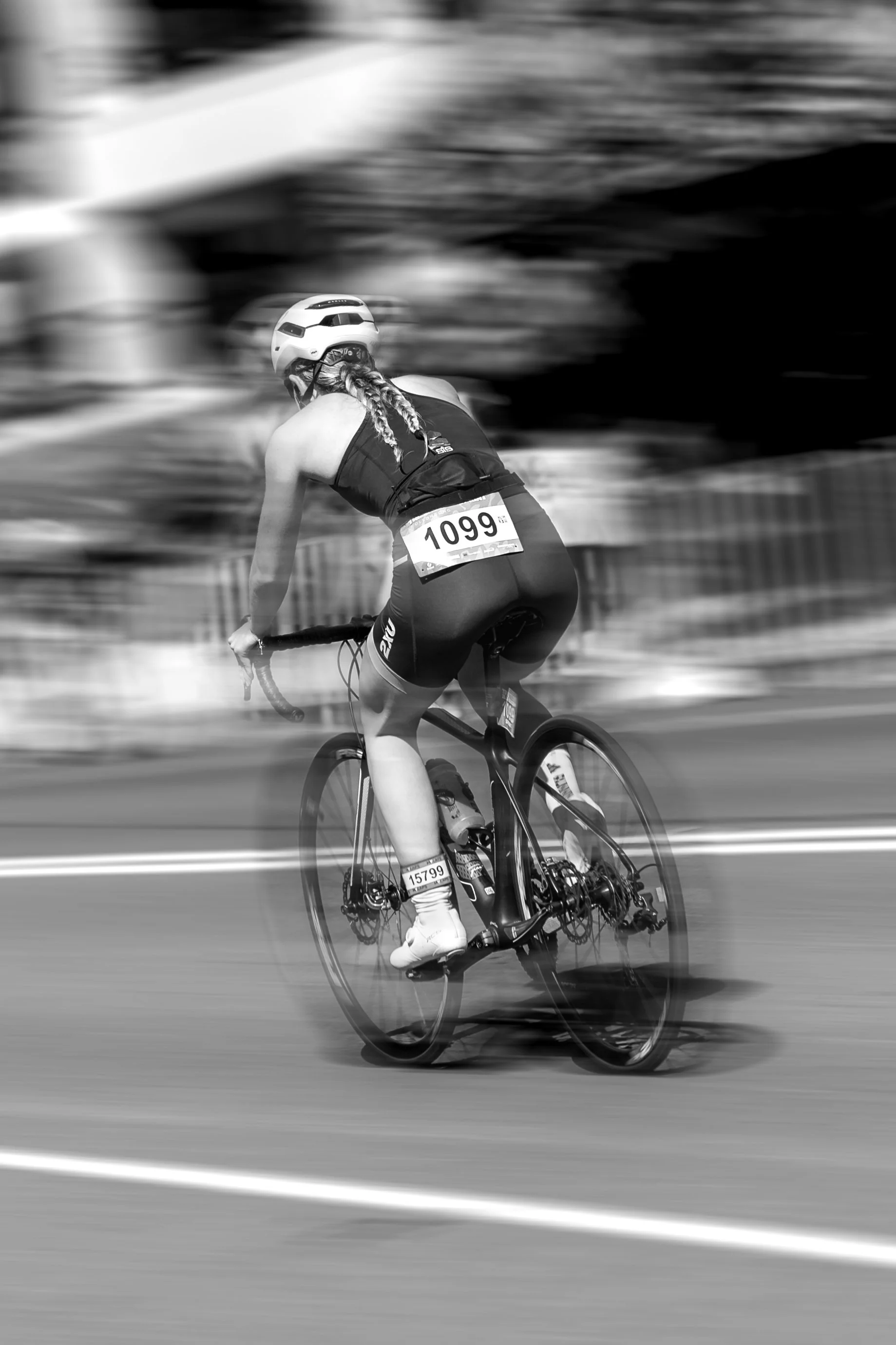 A female cyclist with braided hair, wearing a helmet, riding a bicycle during a race, with blurred background. Wollongong Triathlon 2026 sports photography