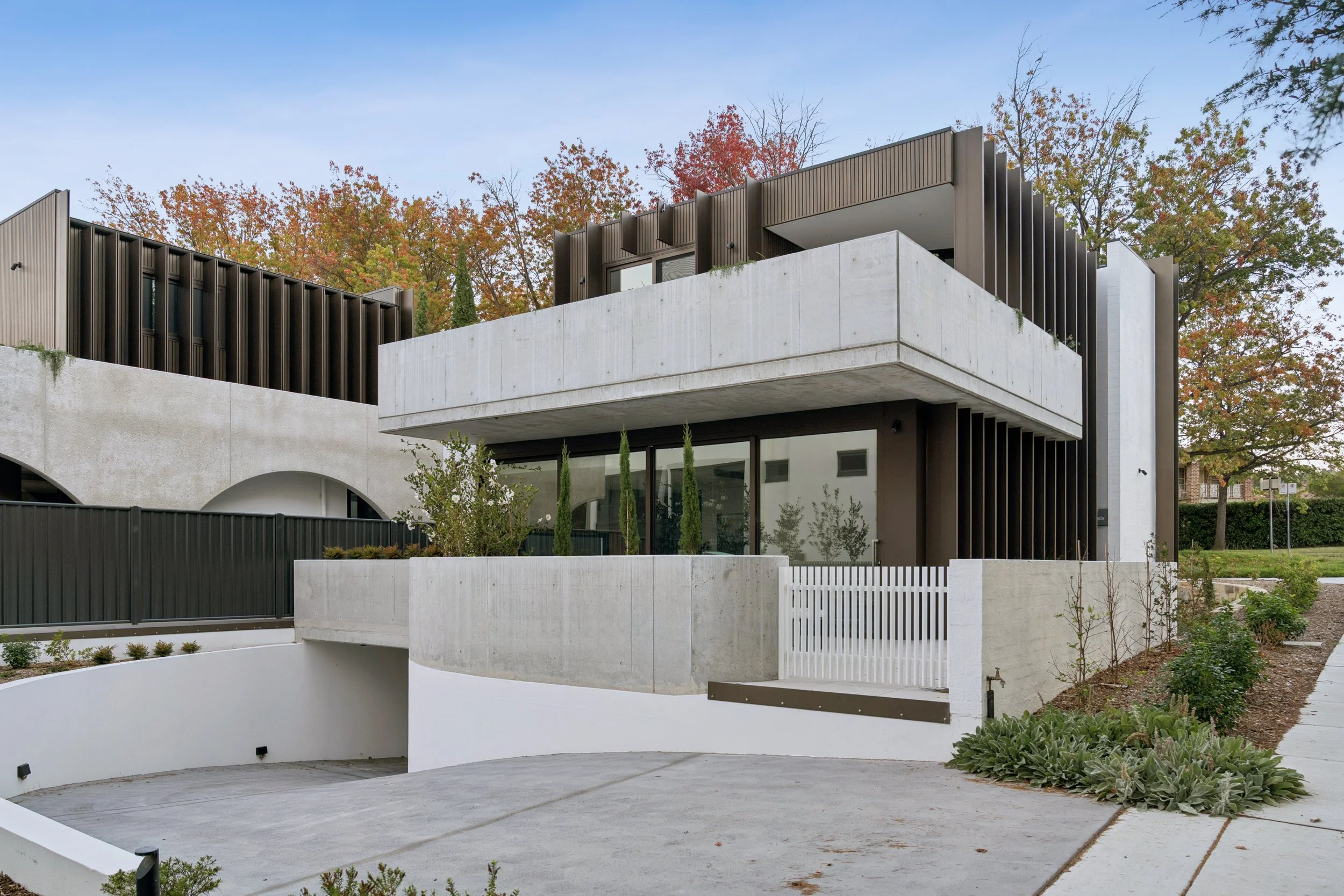 Modern multi-story house with concrete and dark metal exterior, featuring balconies, large windows, architecturally designed home by thursday architecture. real estate editorial photography